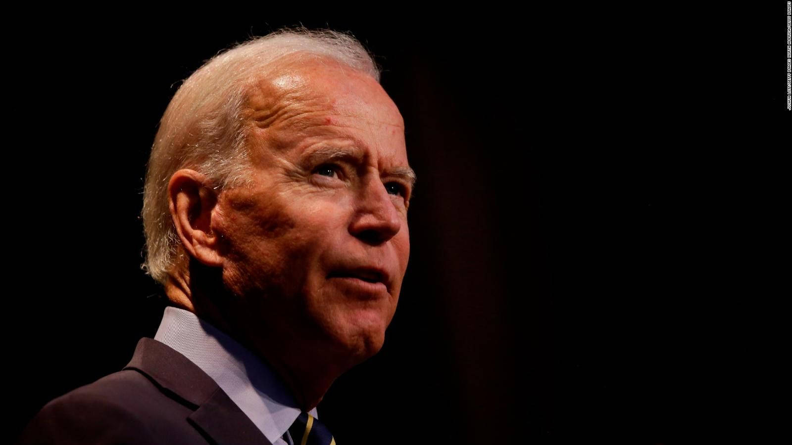 Biden 桌布 壁紙 — 喬·拜登身穿深色西裝，在黑色背景下的特寫肖像，戲劇性的燈光凸顯他的臉部。