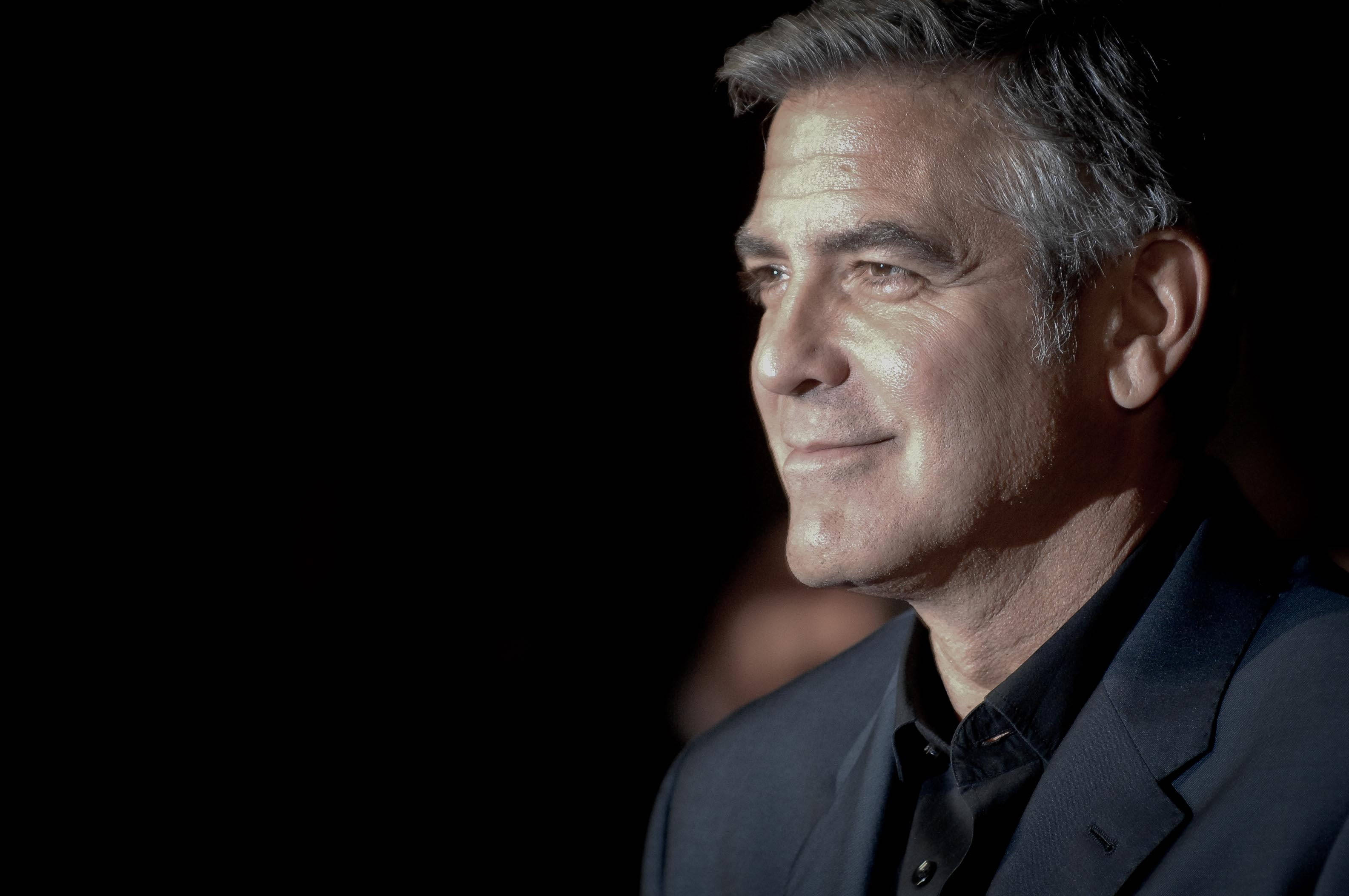 Celebrity 桌布 壁紙 — 喬治克隆尼身穿深色西裝，在黑色背景前拍攝的特寫肖像，戲劇性的燈光凸顯他的臉部。