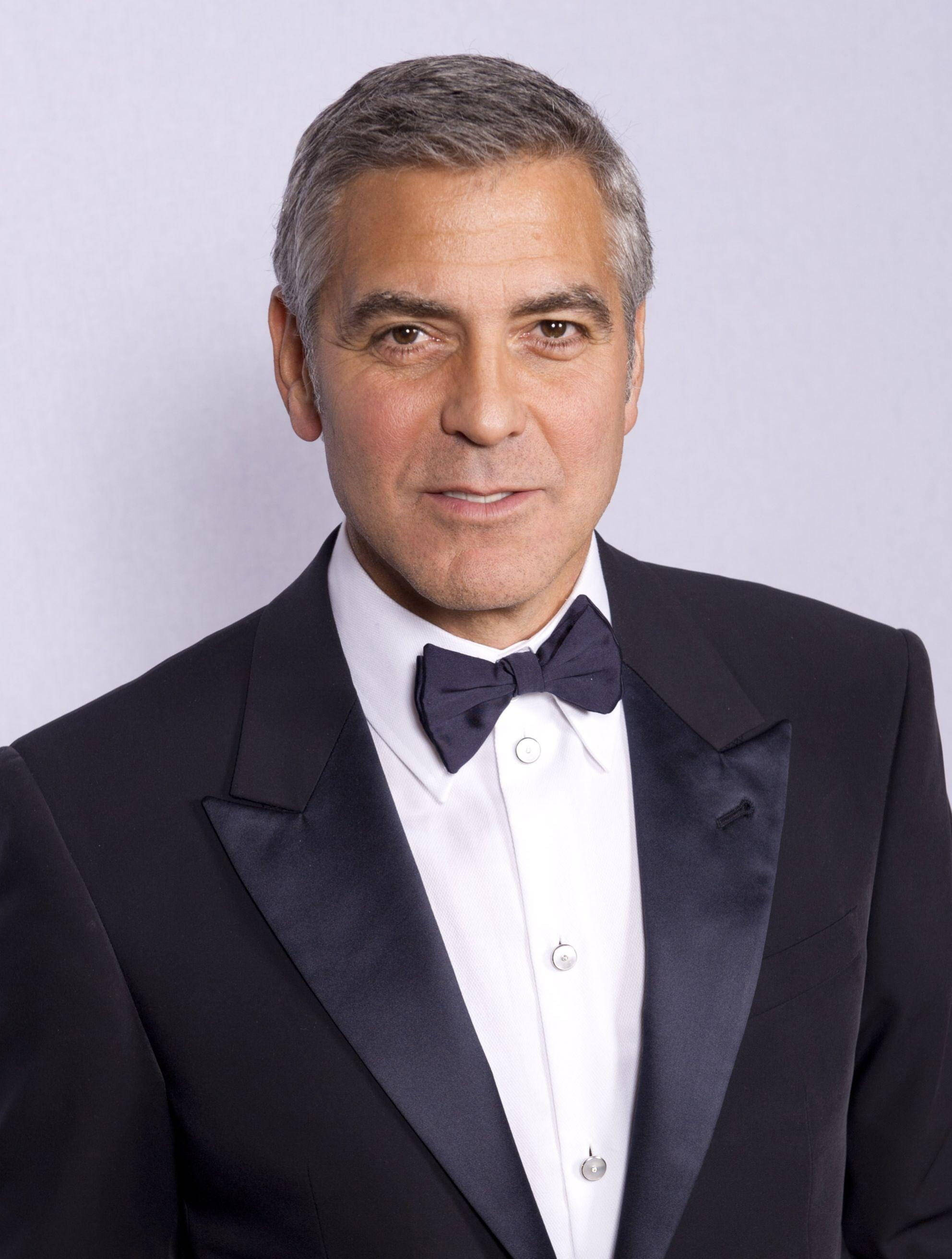 Celebrity 桌布 壁紙 — 喬治克隆尼身穿黑色修身燕尾服配蝴蝶結，在純淺灰色背景前自信地擺姿勢。