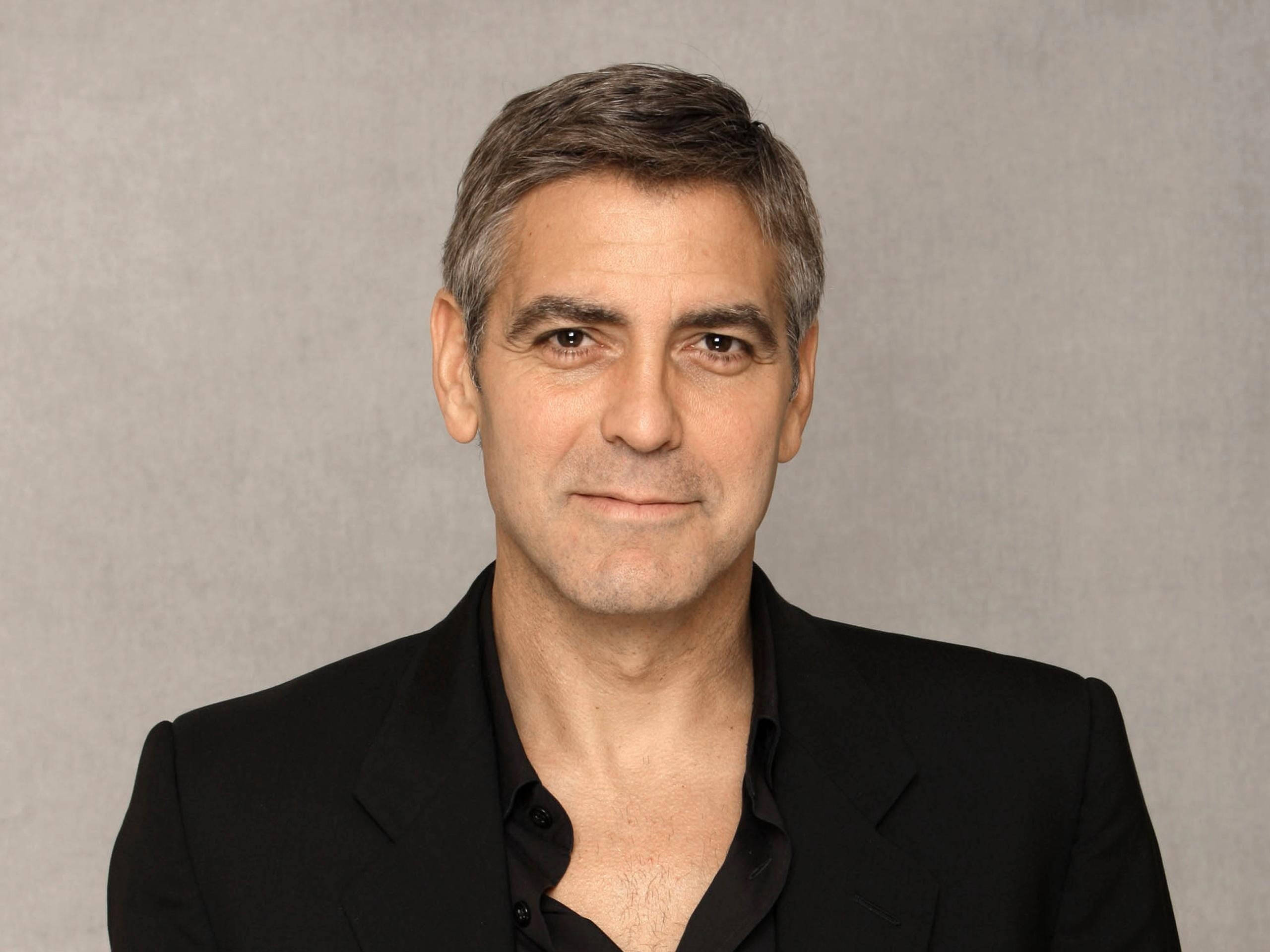 actor 桌布 壁紙 — 喬治克隆尼身穿黑色西裝和襯衫，在柔和燈光下以中性灰色攝影棚背景為襯托。