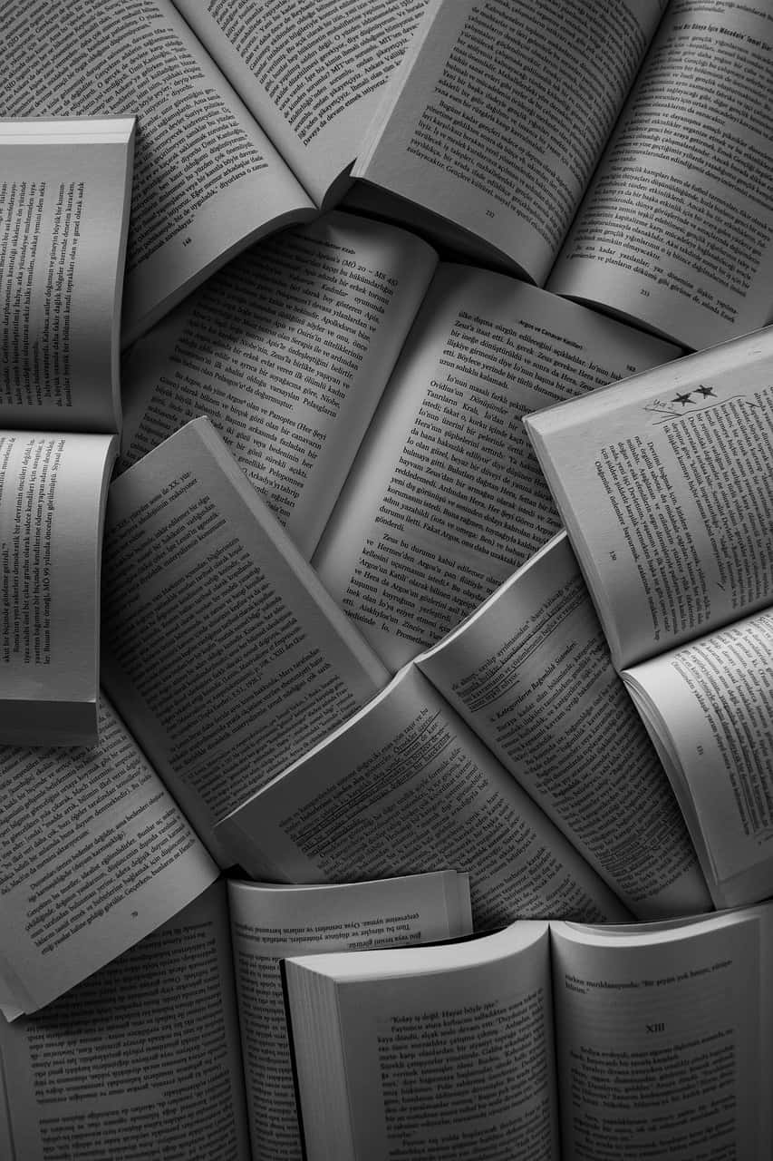 Black And White Book 桌布 壁紙 — 單色俯視圖，散落的打開的書籍，可見的文字頁面，形成有紋理的文學拼貼。