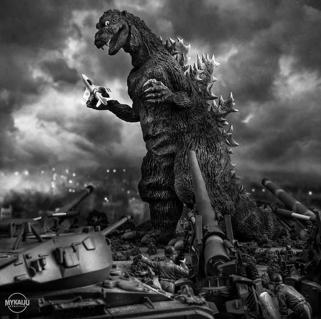 Godzilla 1954 桌布 壁紙 — 單色哥斯拉站在坦克和士兵之中，手持一架微型噴射機，背景是暴風雨的天空。