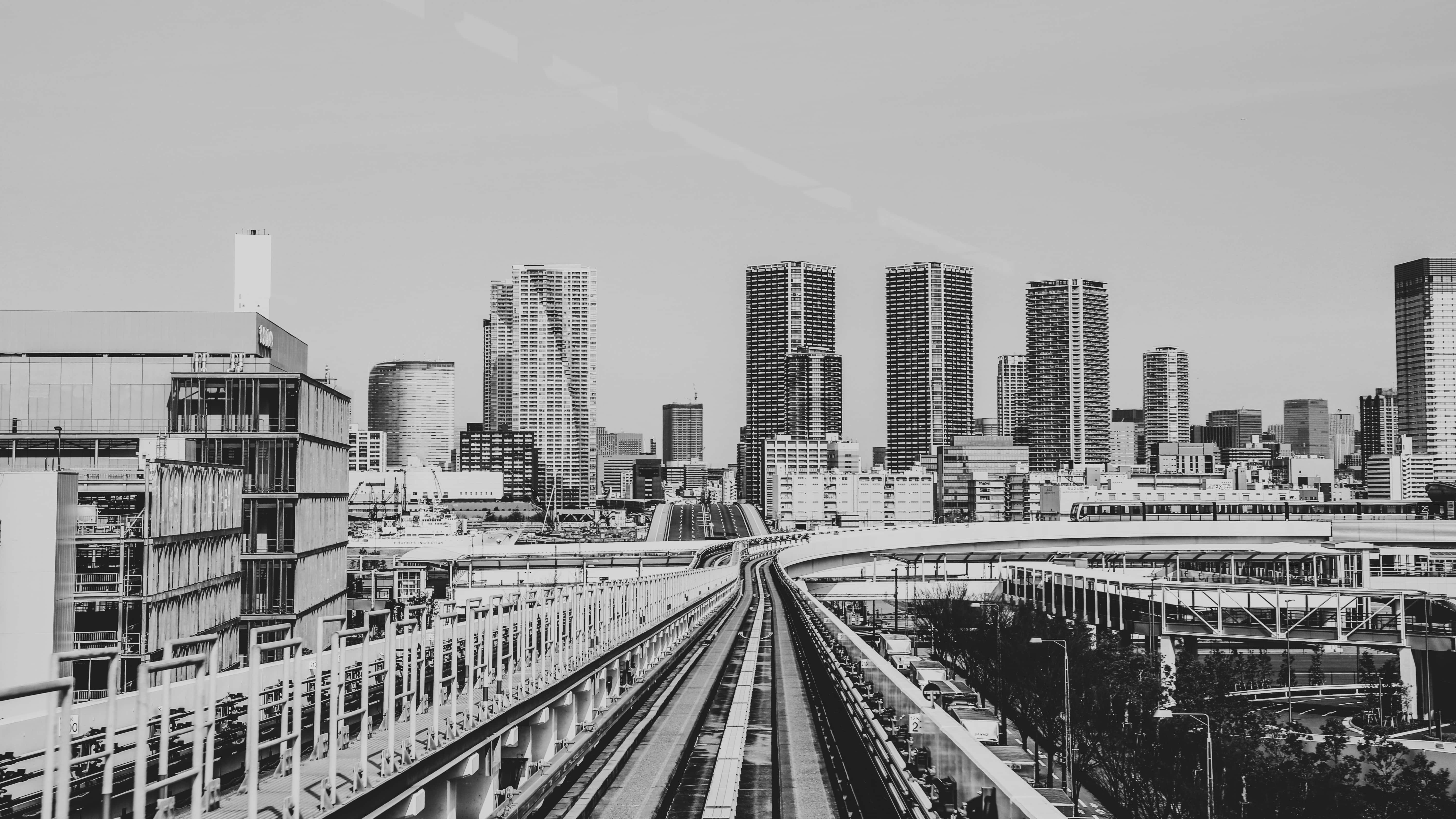 火車 桌布 壁紙 — 單色城市景觀，高架火車軌道匯聚，通向密集的現代摩天大樓天際線。