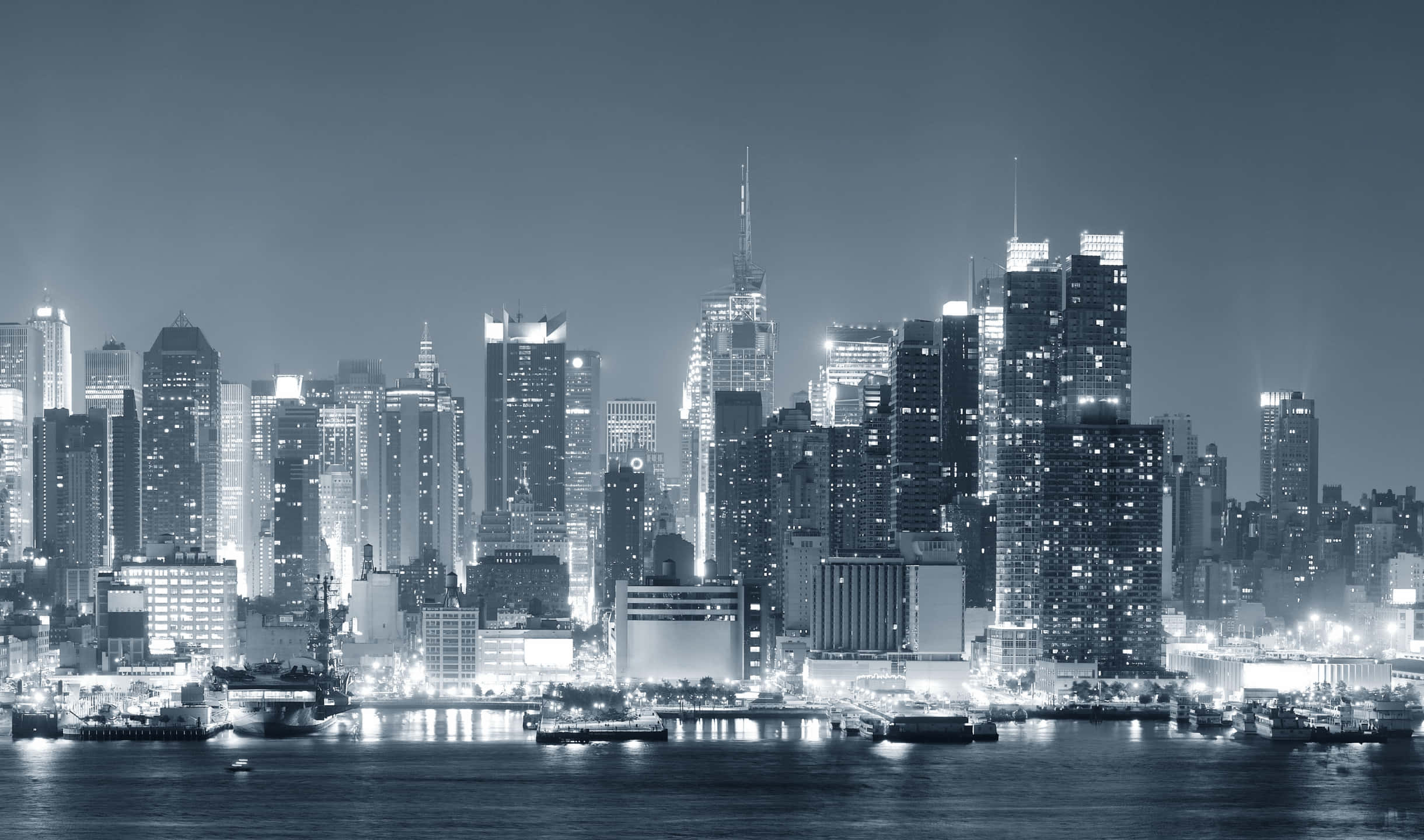 2440x1440 Monitor 桌布 壁紙 — 單色夜景，密集的城市天際線，閃爍的摩天大樓倒映在平靜的水面上。