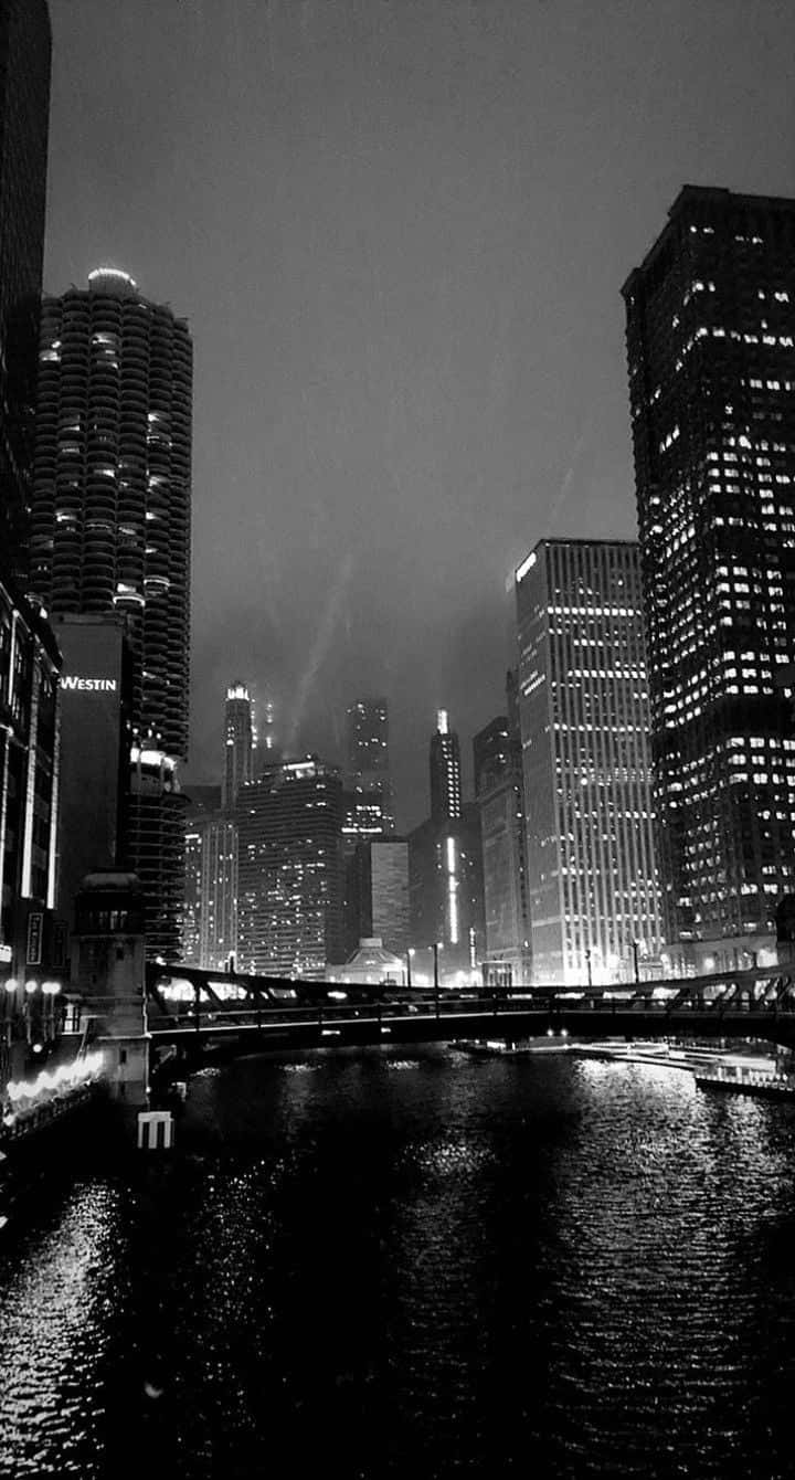 Aesthetic Dark 桌布 壁紙 — 單色夜景城市景觀，高聳的摩天大樓將燈光反射在下面的河流上。
