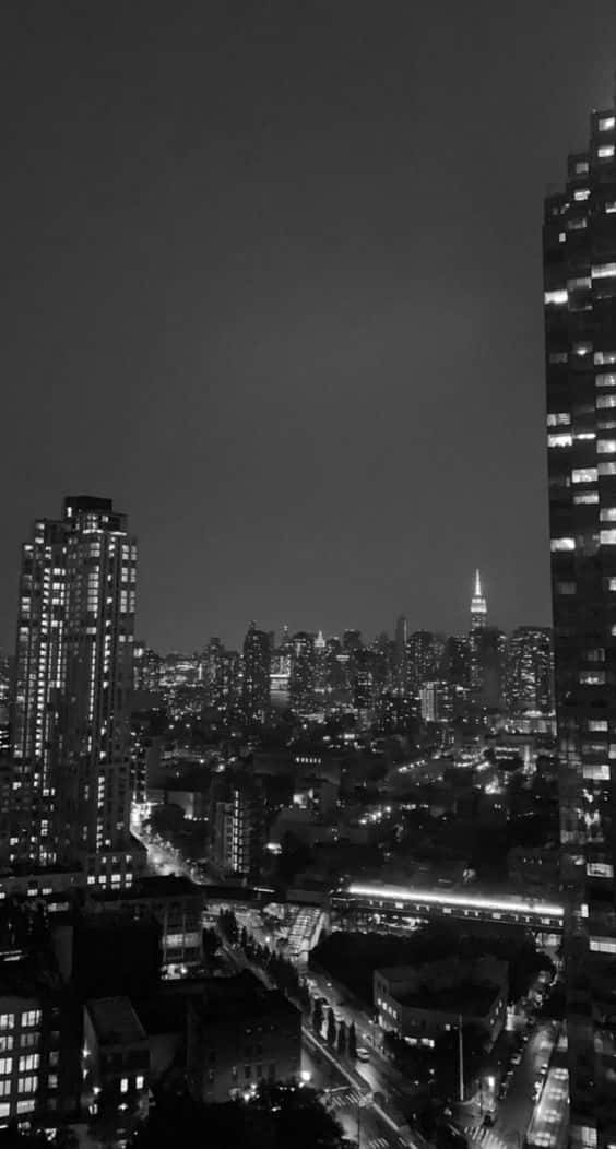 黑白 桌布 壁紙 — 單色夜景城市景觀，高聳的摩天大樓和發光的窗戶映襯著黑暗的天空。