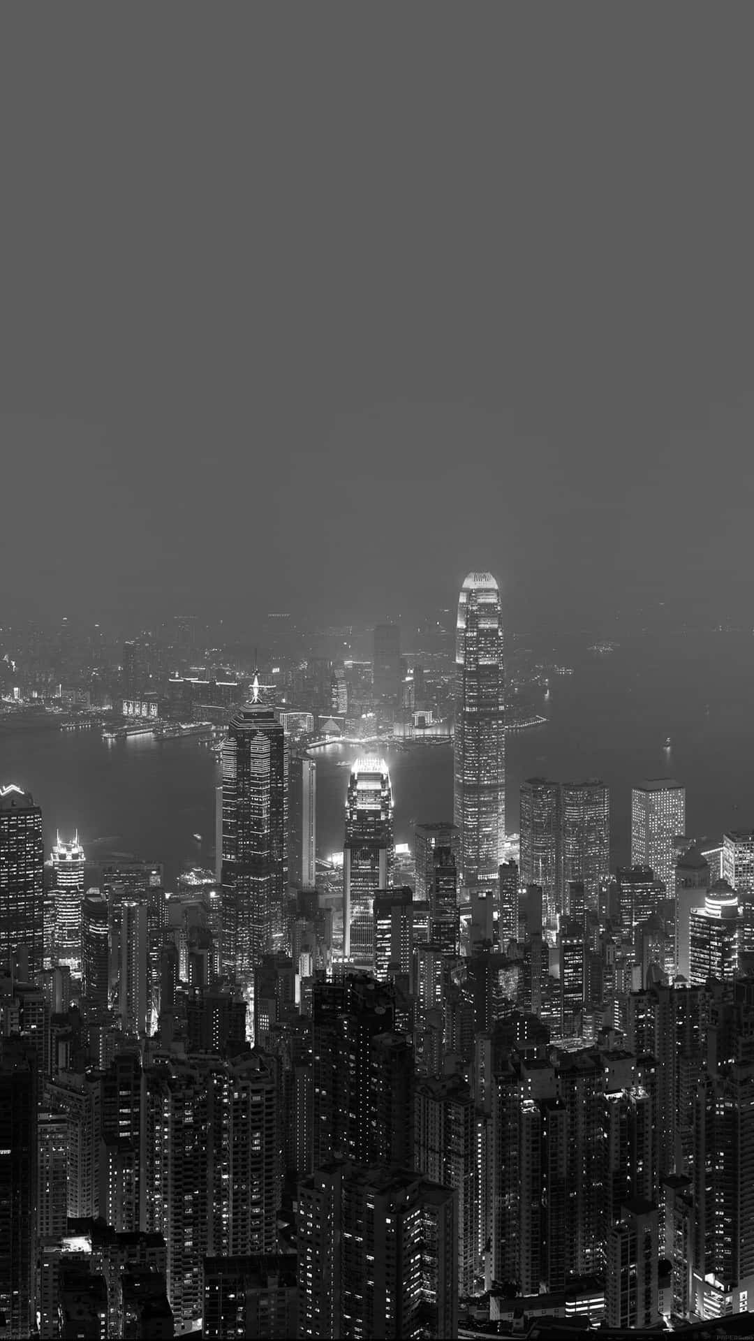 黑暗城市 桌布 壁紙 — 單色夜間城市景觀，高聳的摩天大樓在朦朧的天空中閃爍著燈光。