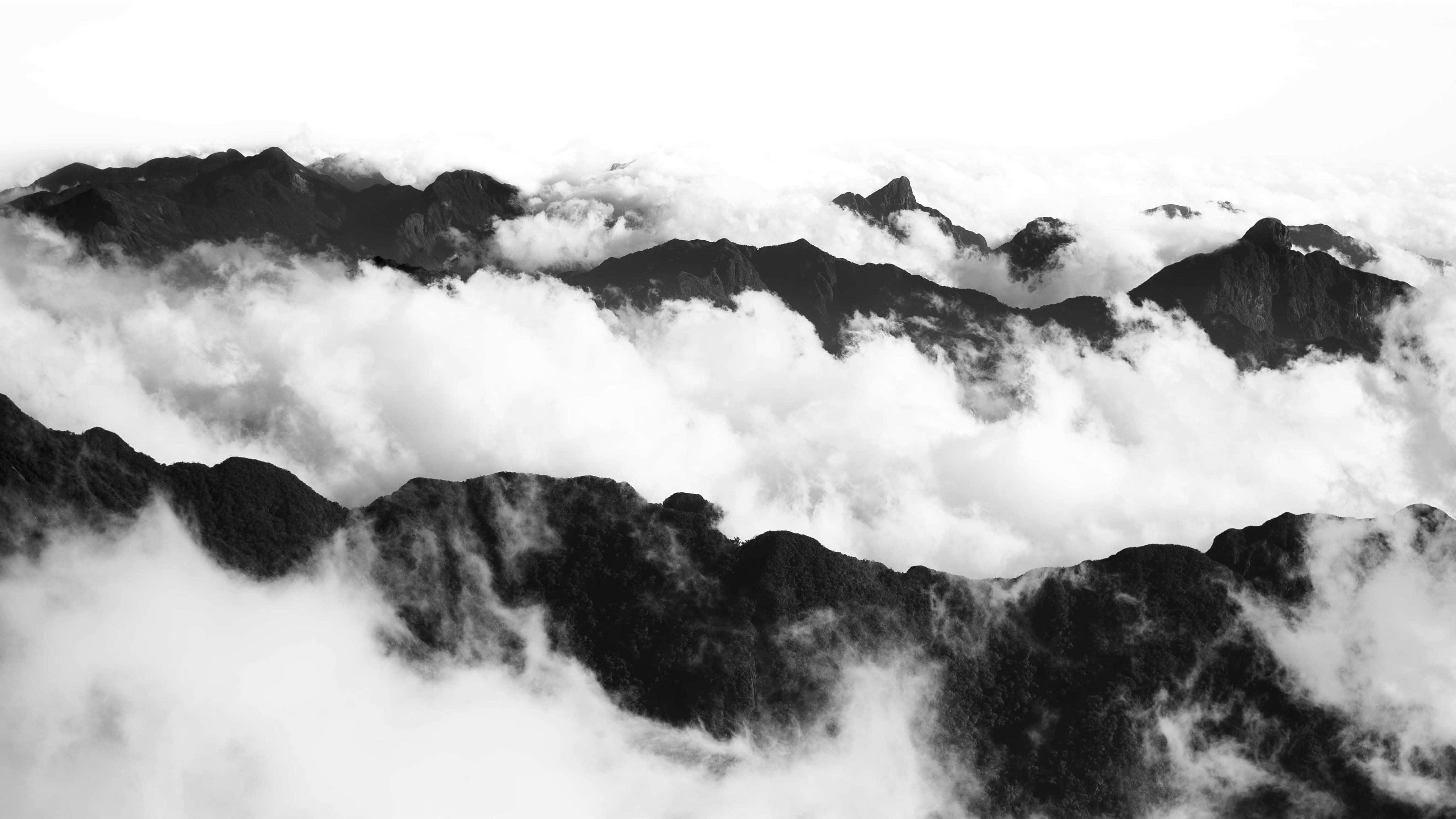Black And White Sky 桌布 壁紙 — 單色山峰穿透旋轉的雲層，呈現戲劇性的高海拔景觀。