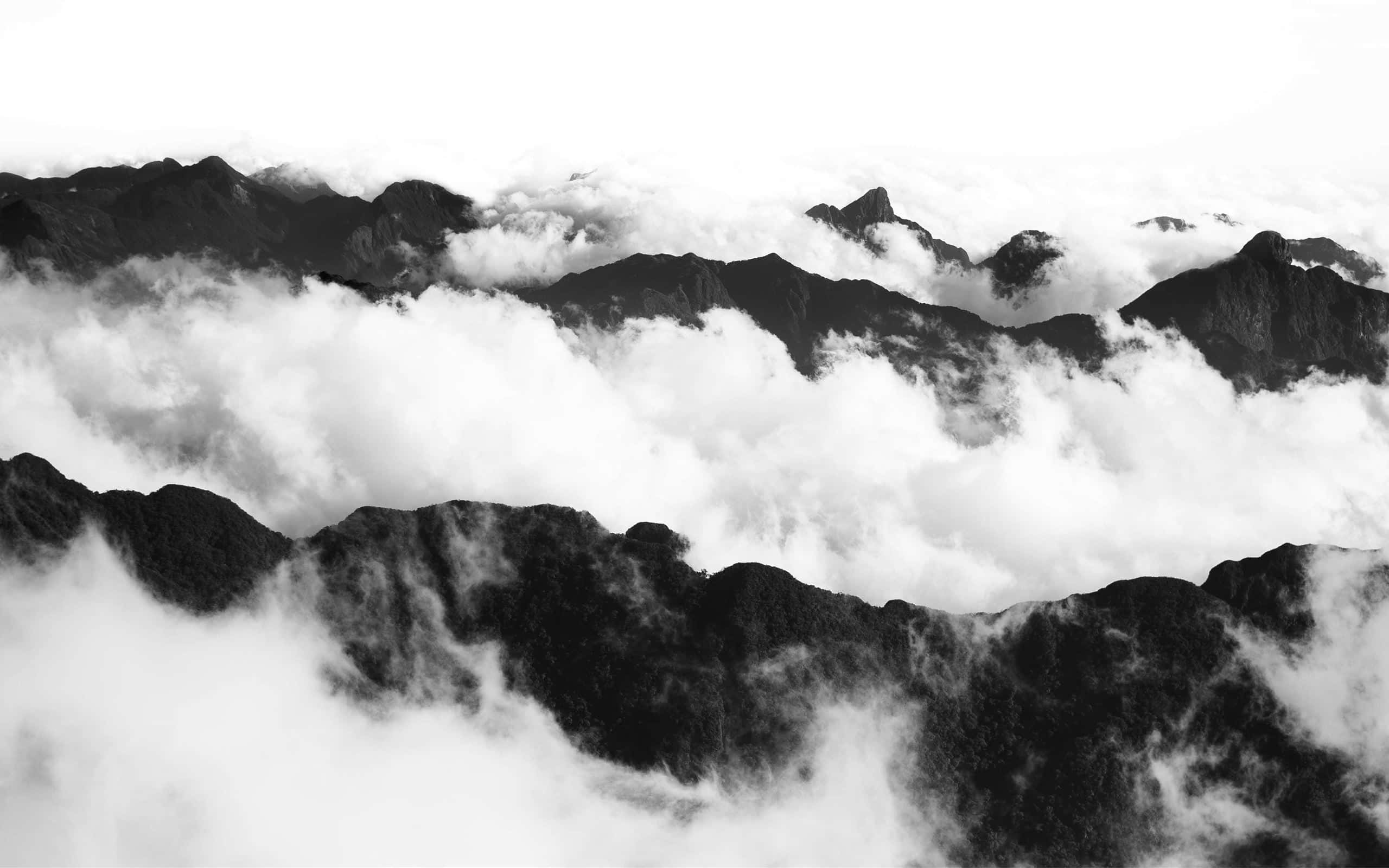 黑白 桌布 壁紙 — 單色山峰穿透濃密雲層，呈現寧靜的高海拔景色。