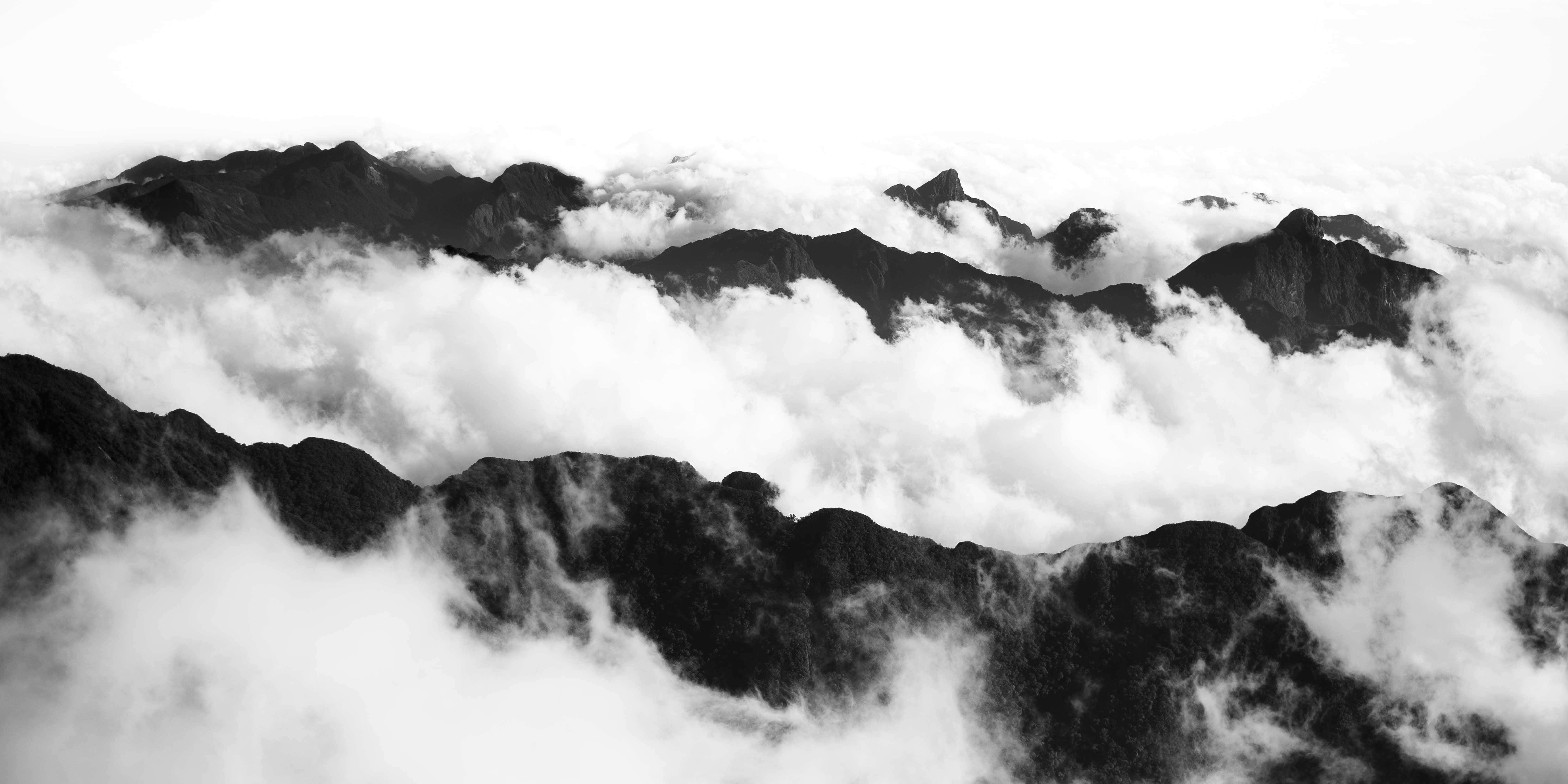 Black And White Landscape 桌布 壁紙 — 單色山峰穿透濃密雲層，呈現戲劇性的高海拔景觀。