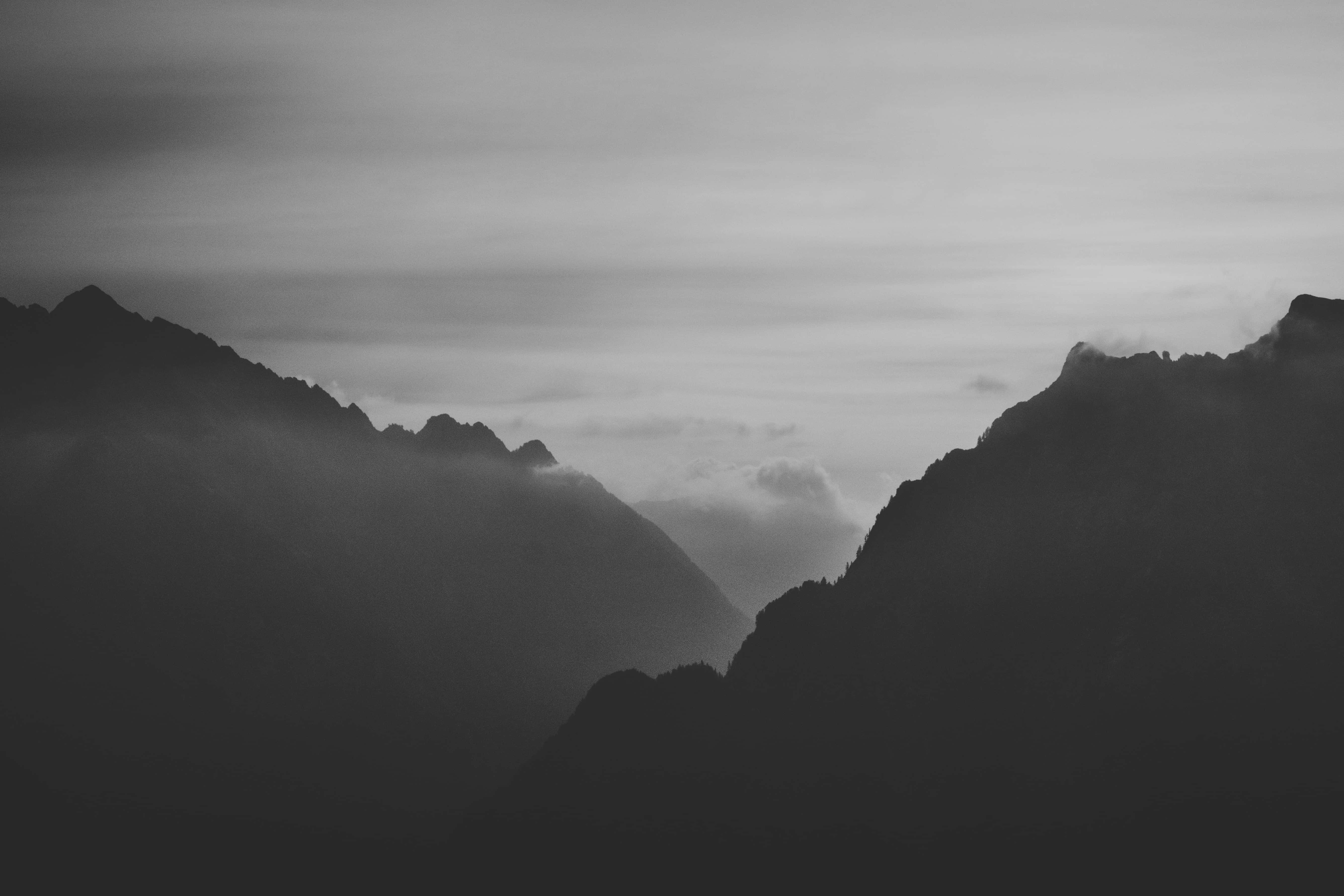 Dark Mountain 桌布 壁紙 — 單色山峰穿透霧氣雲層，呈現寧靜而富有氛圍的景觀。