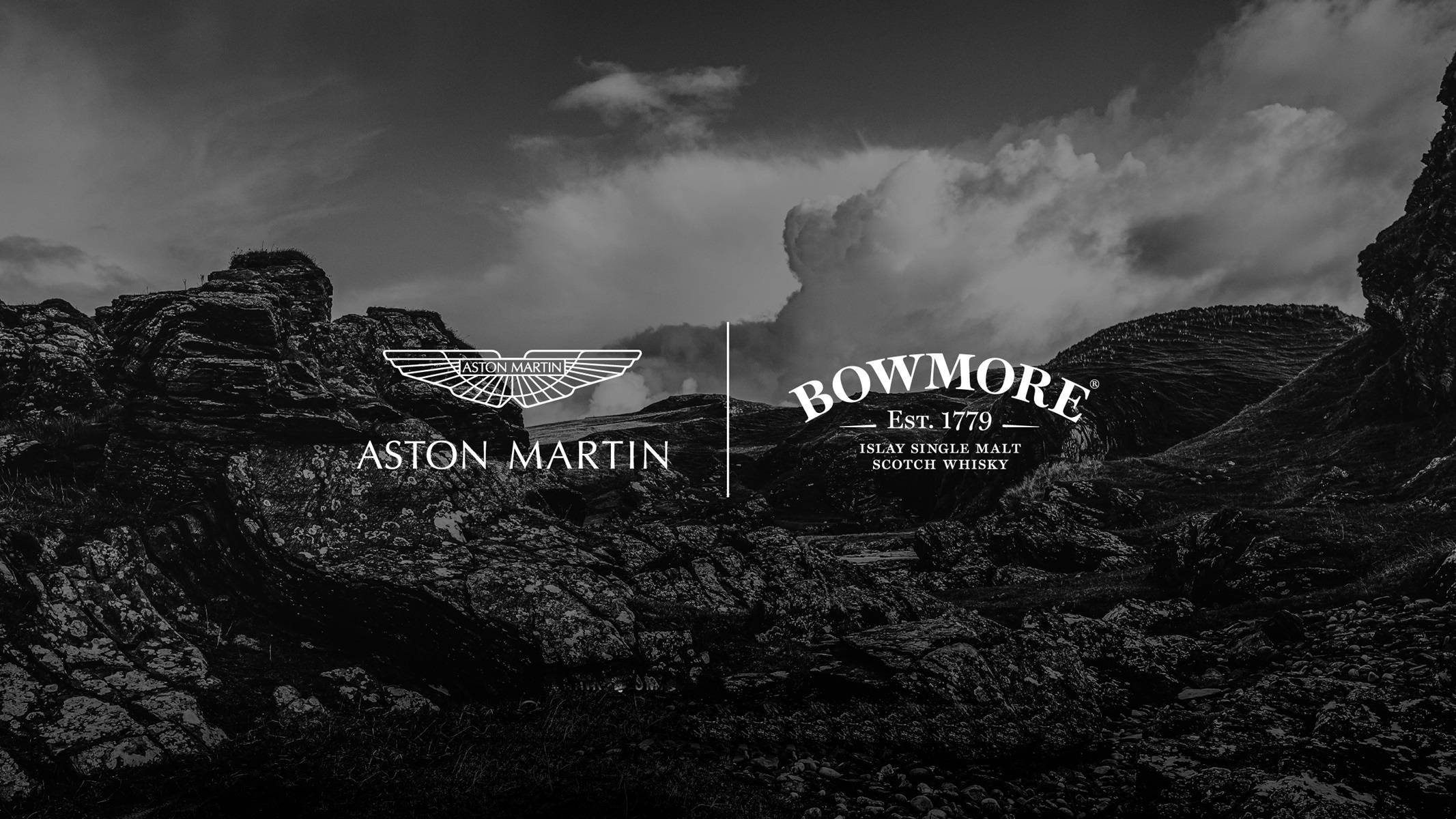 Whiskey 桌布 壁紙 — 單色崎嶇山景，Aston Martin 和 Bowmore 標誌疊加在戲劇性的雲層上。