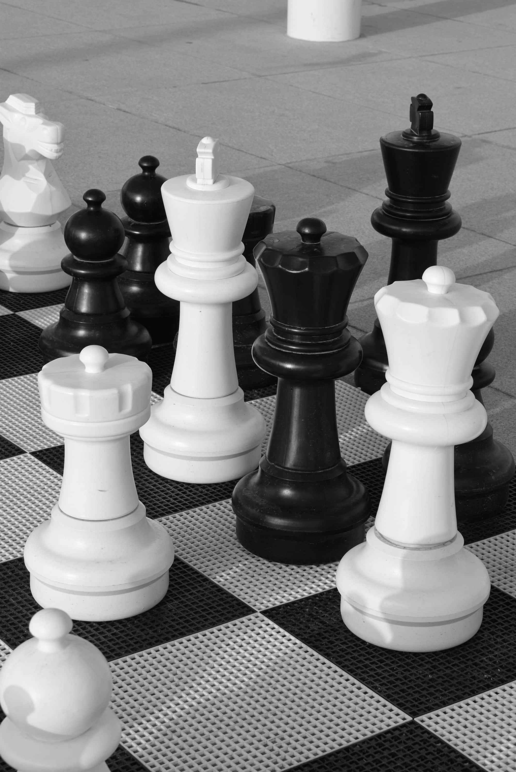 Black And White Chess 桌布 壁紙 — 單色巨型西洋棋棋子矗立在戶外棋盤上，在人行道上投下銳利的陰影。