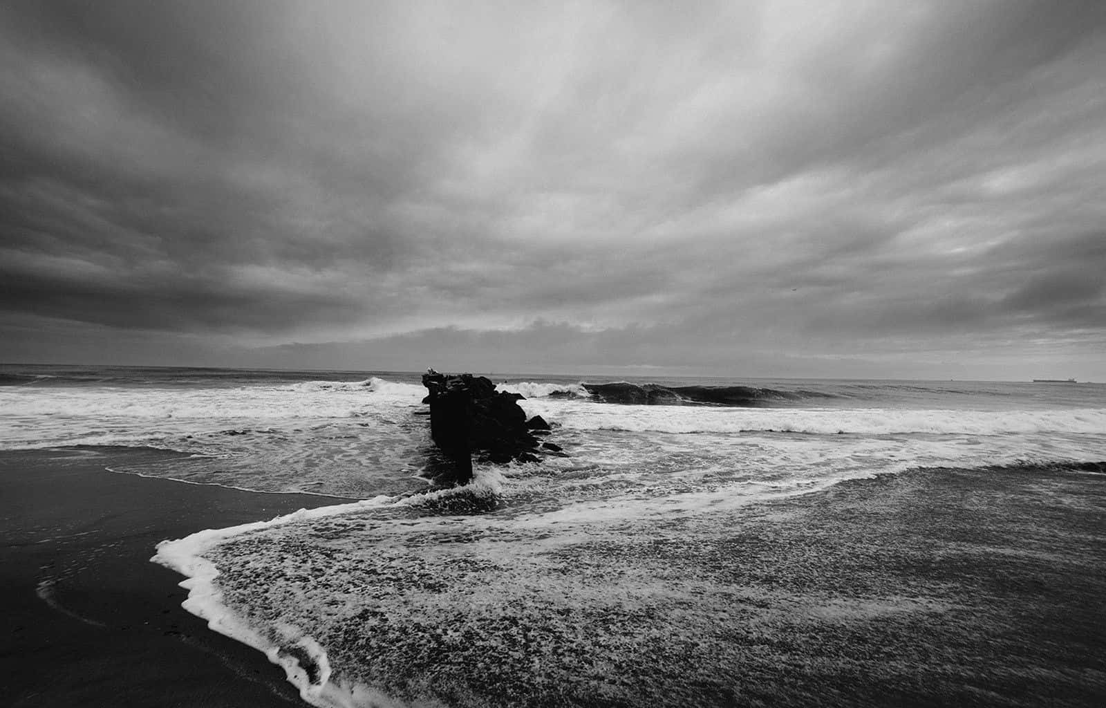 Black And White Ocean 桌布 壁紙 — 單色海浪在厚重陰天的天空下拍打岸邊的黑色岩石。