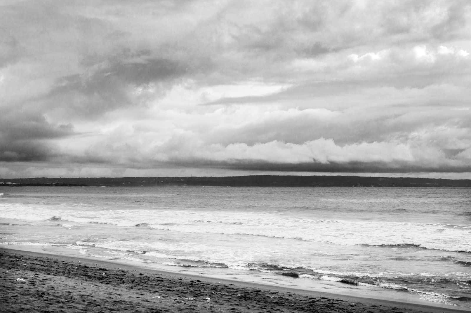 Black And White Ocean 桌布 壁紙 — 單色海灘場景，在戲劇性的多雲天空下，滾滾波浪拍打卵石海岸。
