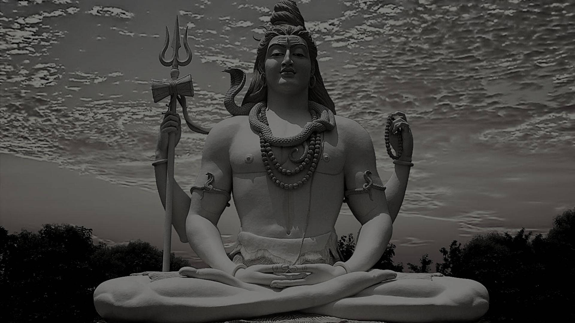 shiva dark 桌布 壁紙 — 單色濕婆雕像，以冥想姿勢手持三叉戟和蛇，背景為多雲天空。