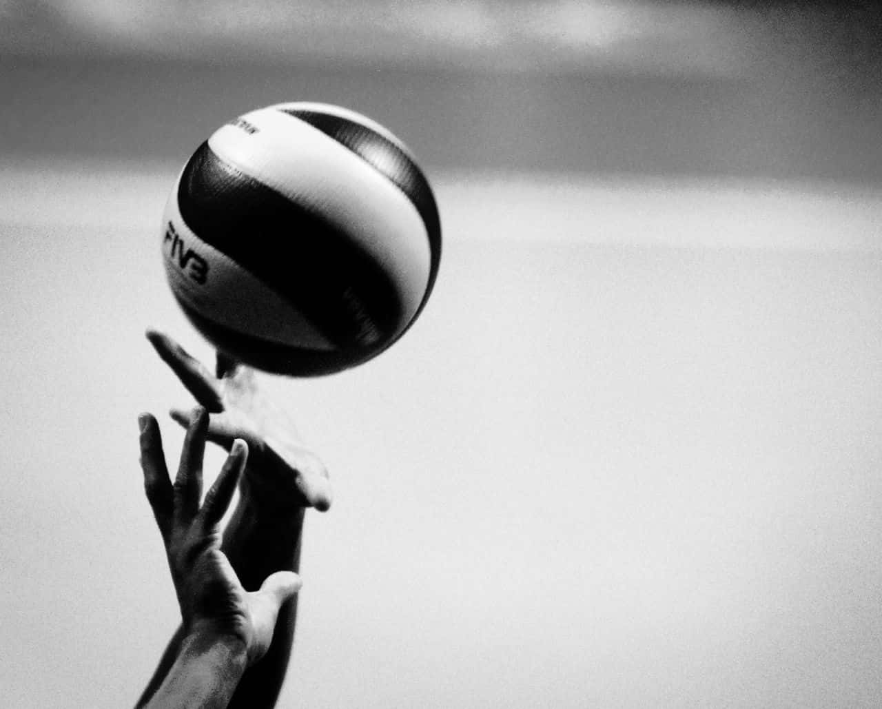 排球 桌布 壁紙 — 單色特寫，雙手在模糊的天空背景下拋擲FIVB排球。