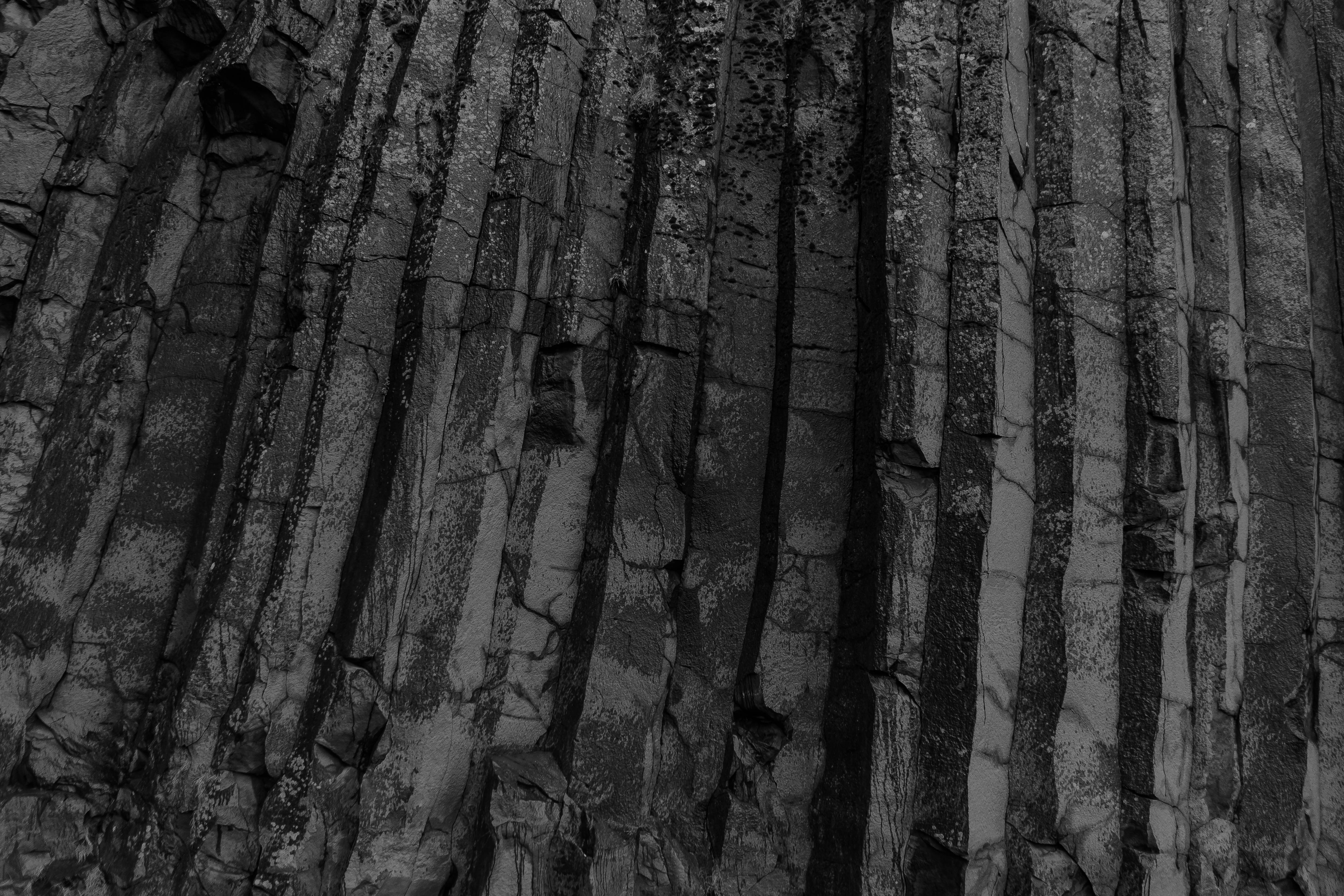simple dark aesthetic 桌布 壁紙 — 單色特寫崎嶇的玄武岩柱，形成帶有深垂直裂縫的戲劇性天然岩面。