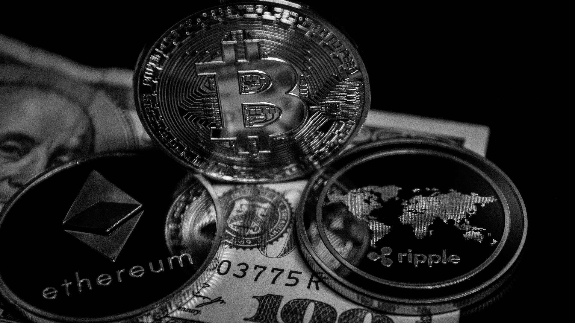 以太坊 桌布 壁紙 — 單色特寫比特幣、以太坊和瑞波幣加密貨幣硬幣堆疊在美元鈔票上，背景為深色。