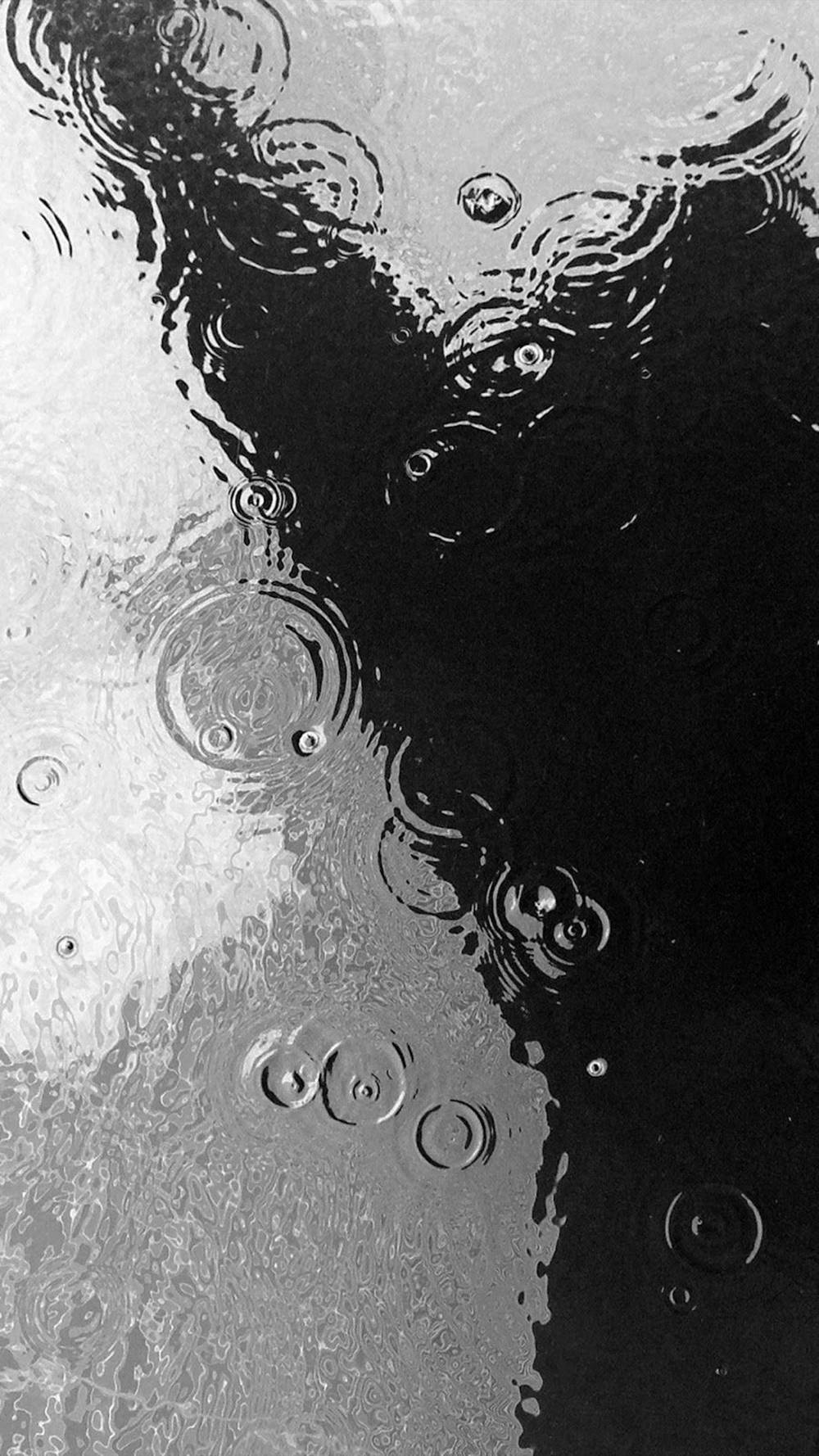 黑白 桌布 壁紙 — 單色特寫雨滴在潮濕玻璃表面形成漣漪，帶有強烈的光影對比。
