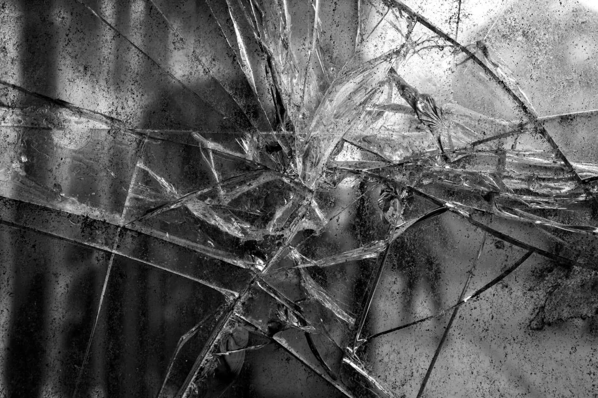 Broken Glass 桌布 壁紙 — 單色調中，從中心撞擊點輻射出複雜裂紋的破碎玻璃表面。