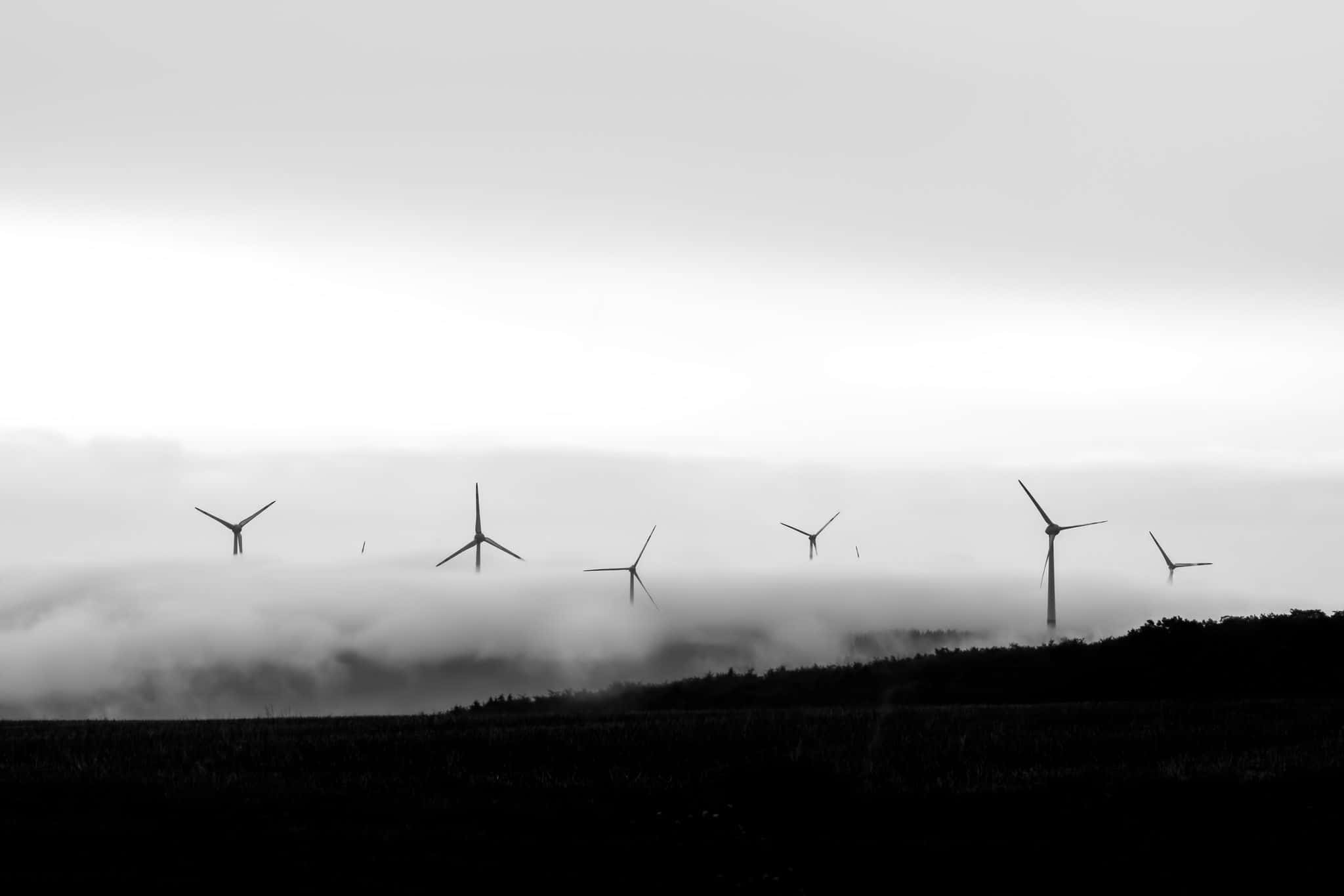 Wind 桌布 壁紙 — 單色調中，風力發電機的剪影在柔和灰色天空下，從霧氣籠罩的山谷中升起。
