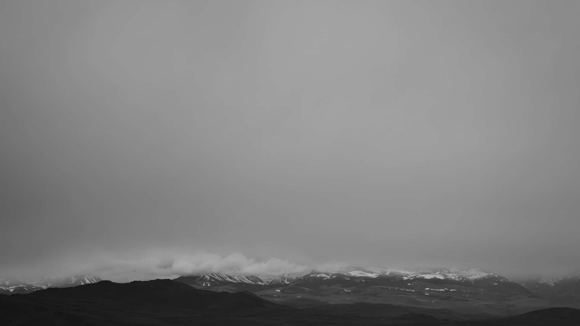 Aesthetic Black And White 桌布 壁紙 — 單色調山脈，積雪的山峰在陰天低垂的雲層中若隱若現。