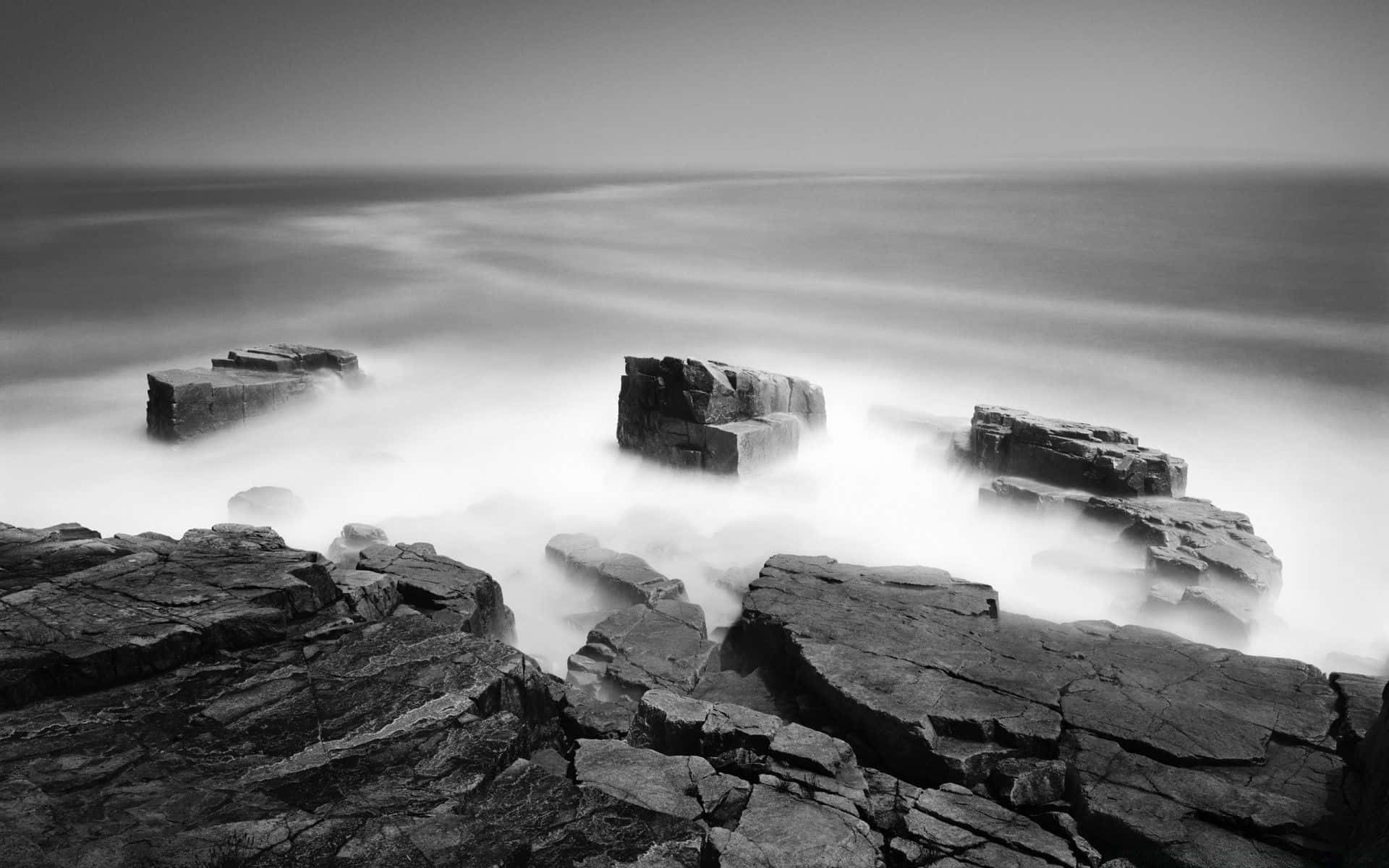 Black And White Ocean 桌布 壁紙 — 單色長時間曝光海景，平滑流動的水在崎嶇海岸岩石周圍旋轉。