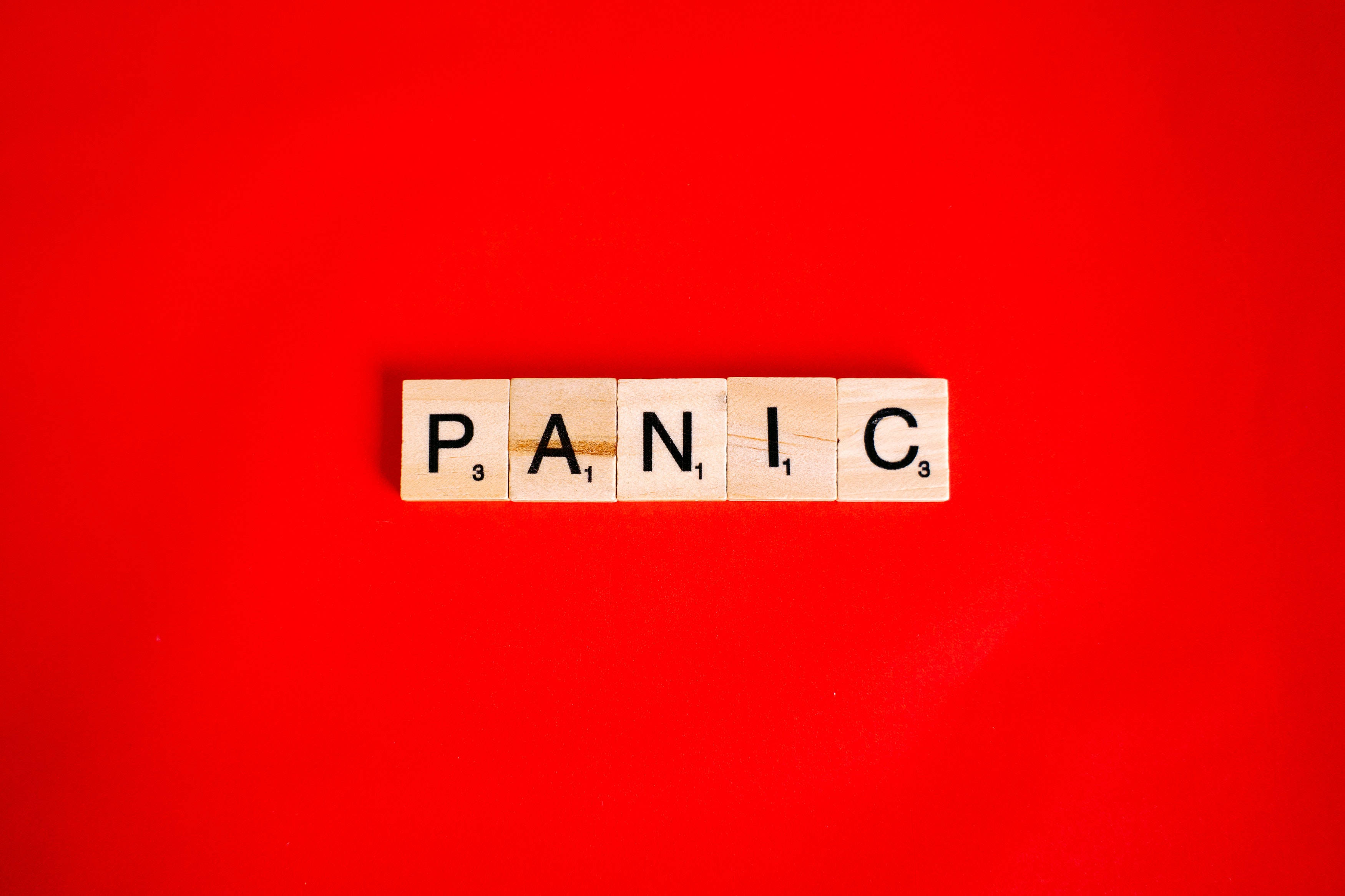 Panic 桌布 壁紙 — 單詞「PANIC」用木製Scrabble字母塊拼出，居中放在鮮紅色背景上。