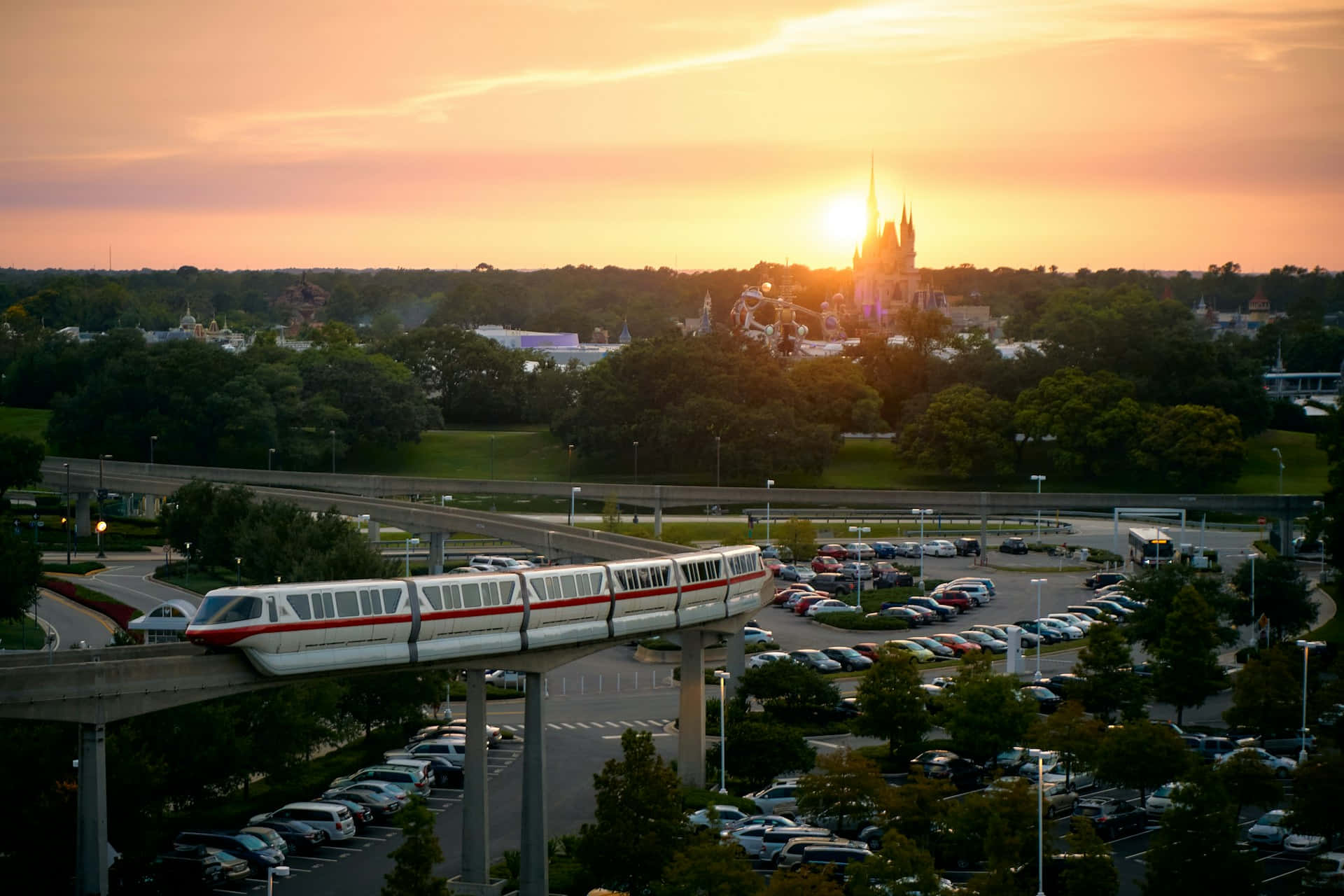 Orlando 桌布 壁紙 — 單軌列車在停車場上空滑行，夕陽在灰姑娘城堡後方散發出溫暖的金色光芒。