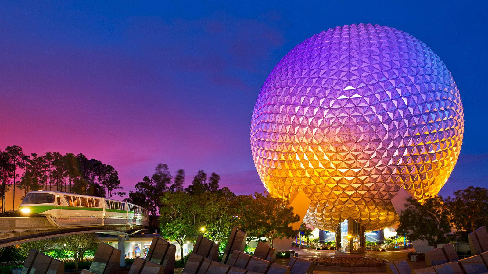 漸層 桌布 壁紙 — 單軌列車在黃昏時掠過發光的測地線球體Spaceship Earth，天空呈現紫色和橙色。