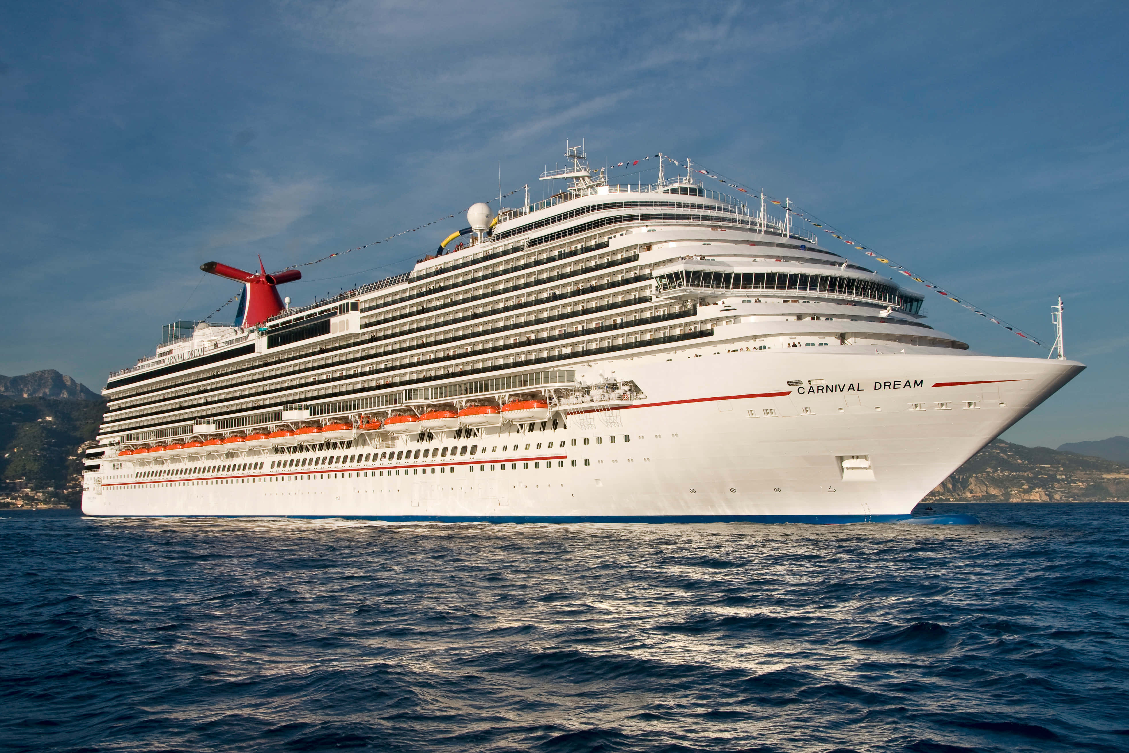 Carnival Dream 桌布 壁紙 — 嘉年華夢想號郵輪在清澈的天空下優雅地航行在深藍色的水域上，背景是遙遠的山脈。