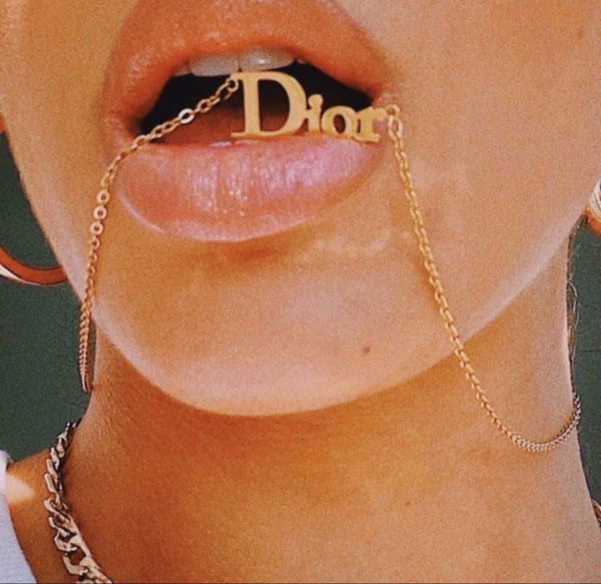 Dior 動態 桌布 壁紙 — 嘴唇含住一條金色Dior鏈條項鍊，帶有醒目標誌吊墜的特寫。