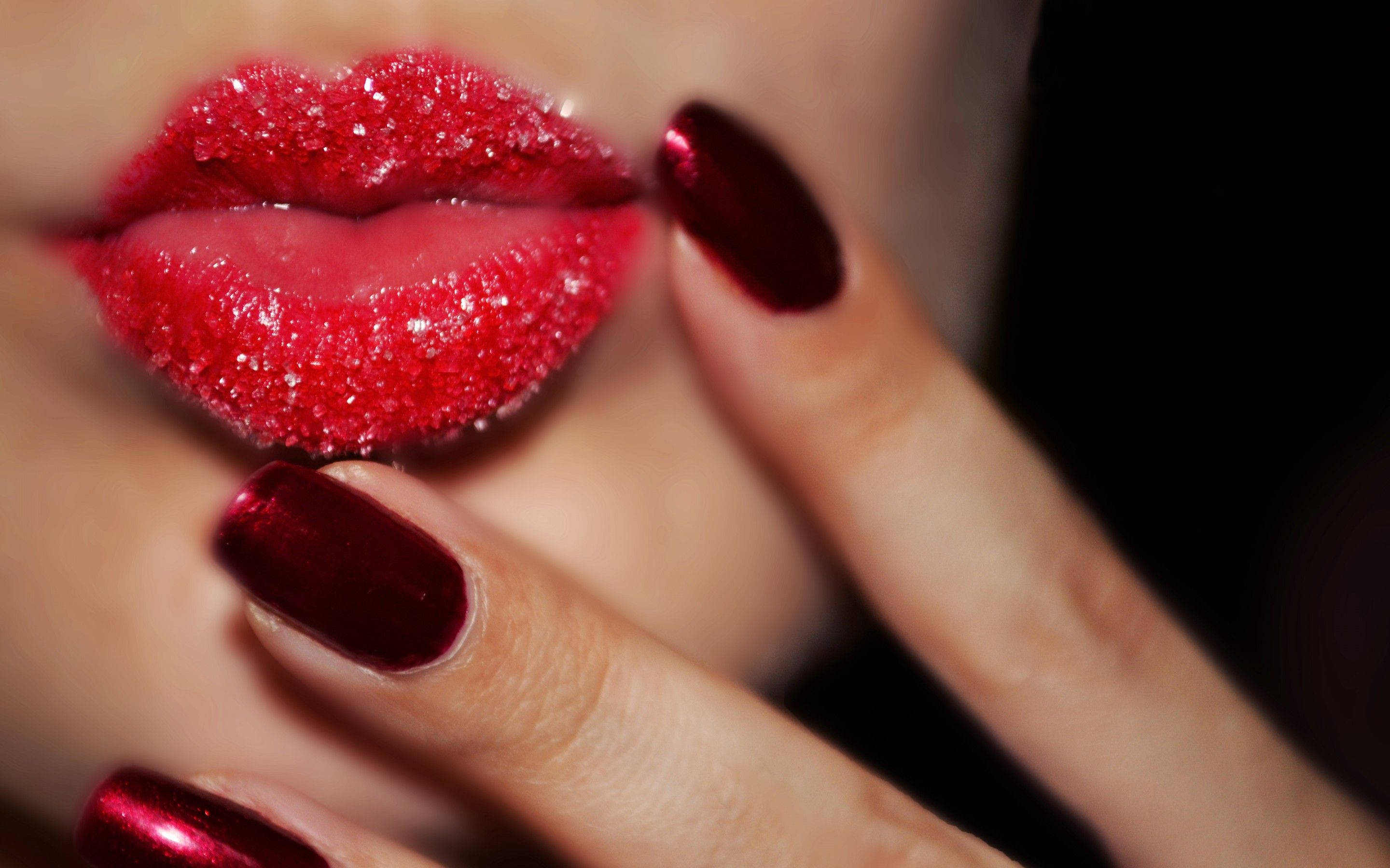 red lips 桌布 壁紙 — 嘴唇和手指的特寫，飾有閃亮的紅色化妝品和相配的指甲，背景為深色。