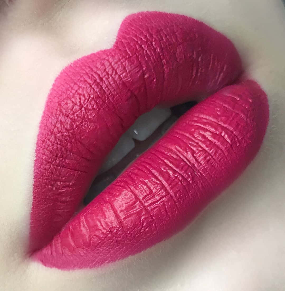 Pink Lipstick 桌布 壁紙 — 嘴唇特寫，塗上充滿活力的紫紅色啞光唇膏，展現細膩肌膚紋理和牙齒上的微妙光澤。