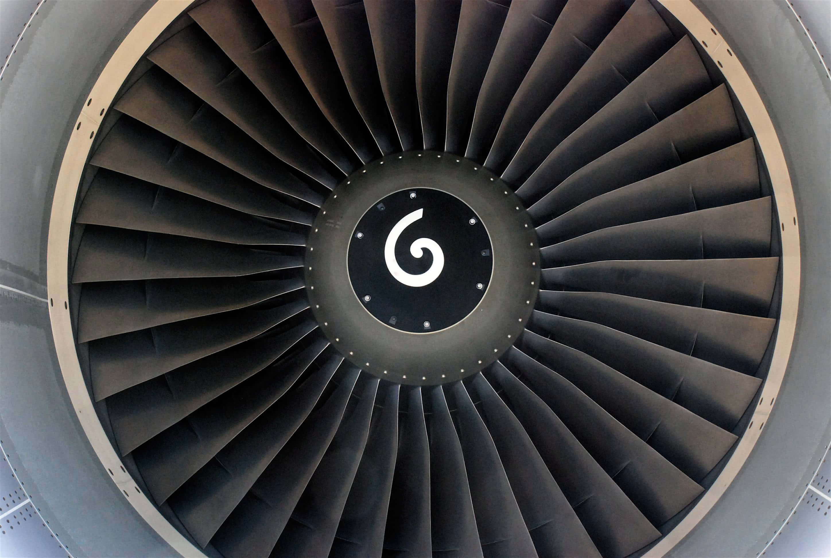 Jet Engine 桌布 壁紙 — 噴射引擎風扇葉片特寫，中央有漩渦標誌，背景為金屬灰和黑色色調。
