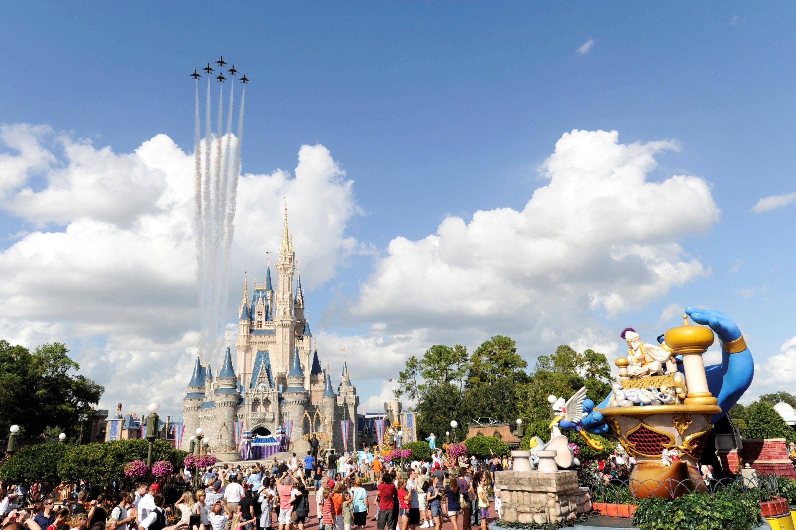 Theme Park 桌布 壁紙 — 噴射機在灰姑娘城堡上空留下煙霧痕跡，人群在點綴著蓬鬆雲朵的明亮藍天下歡呼。