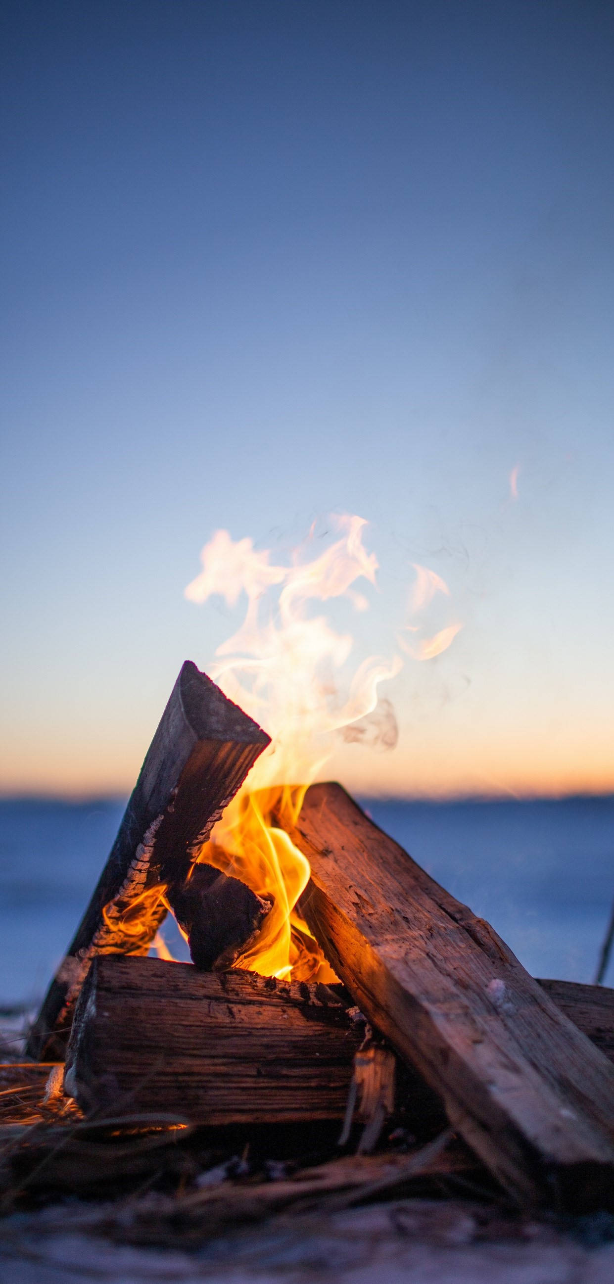 Flames 桌布 壁紙 — 噼啪作響的營火在海灘上日落時分明亮地燃燒，溫暖的光芒映照在清涼的藍色天空和海洋地平線上。