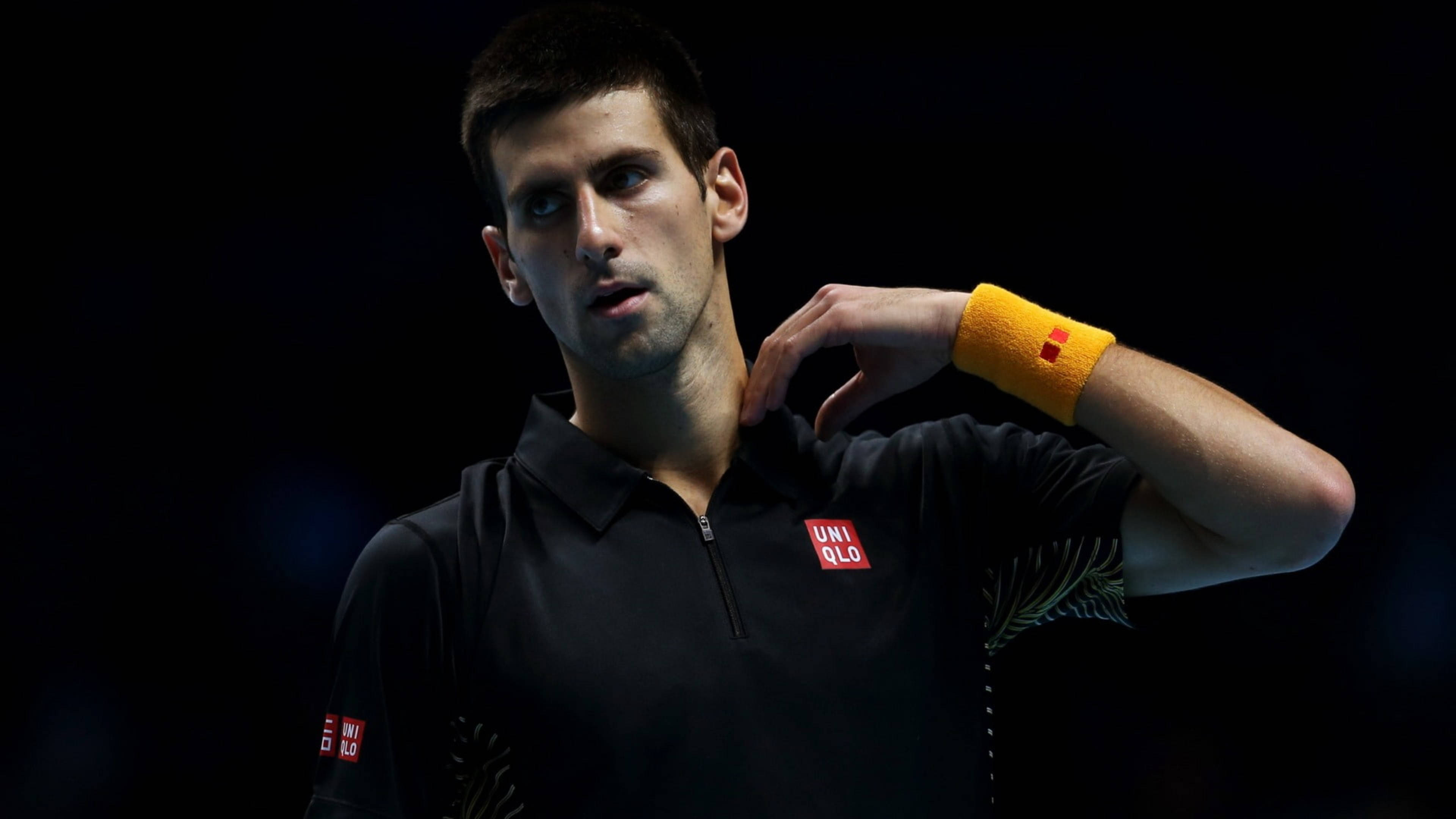 Novak 桌布 壁紙 — 嚴肅的網球選手Novak Djokovic穿著黑色Uniqlo襯衫和黃色腕帶，背景深色。