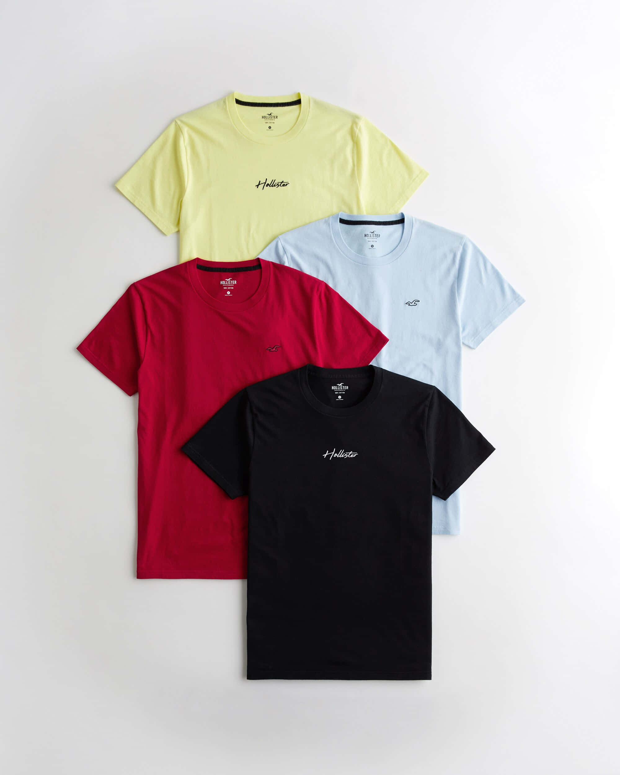 Hollister 桌布 壁紙 — 四件色彩繽紛的Hollister T恤，分別為黃色、紅色、淺藍色和黑色，整齊排列在純白色背景上。