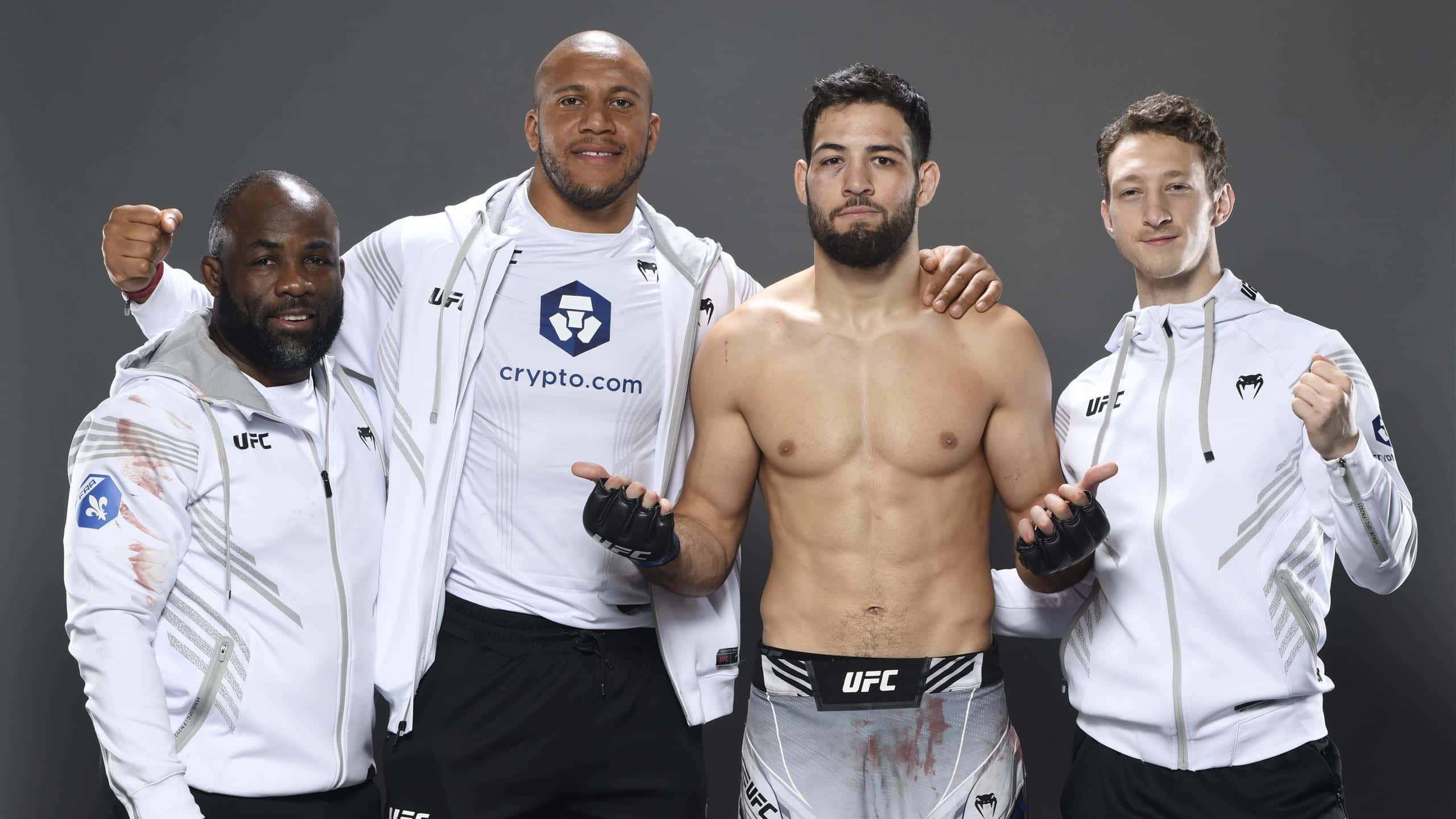 MMA 桌布 壁紙 — 四位UFC拳手在攝影棚自信擺姿勢，中間一位赤裸上身，兩側三位身穿白色品牌外套。