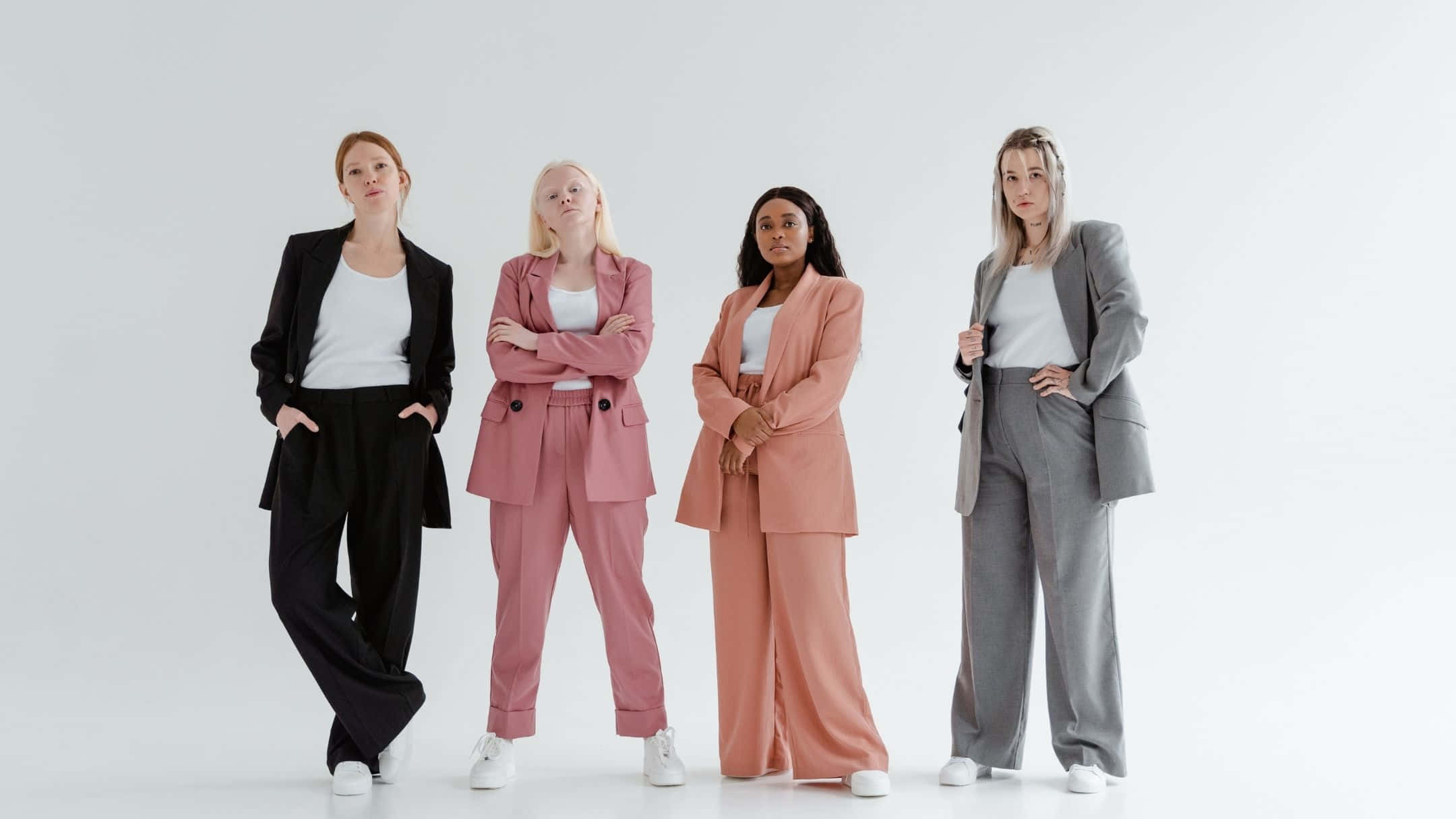women 桌布 壁紙 — 四位不同風格的女性穿著時尚西裝外套和寬褲，在純白工作室背景前自信地擺姿勢。