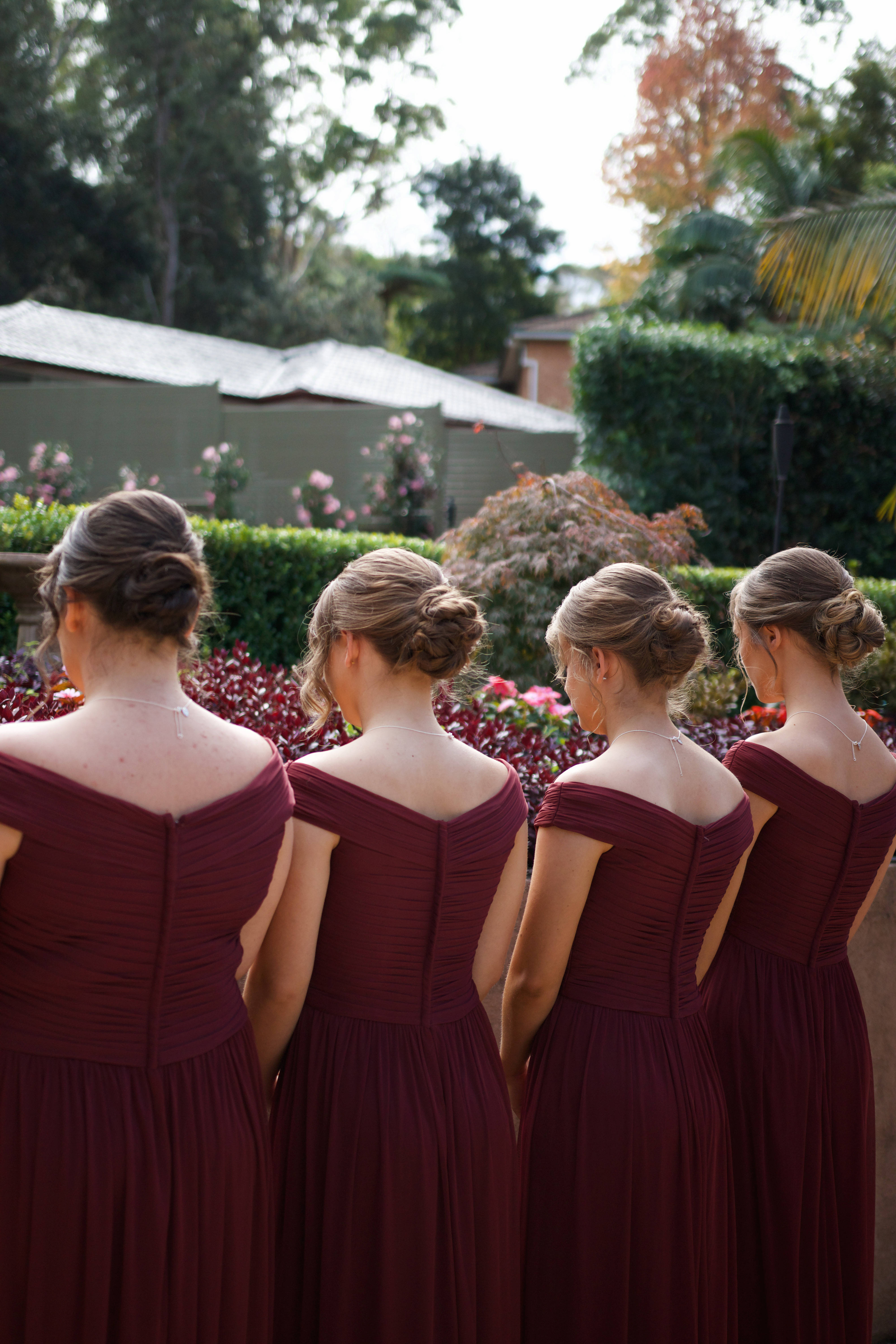 Bridesmaids 桌布 壁紙 — 四位伴娘穿著相配的酒紅色露肩禮服，在茂盛的花園中背對鏡頭站成一排。