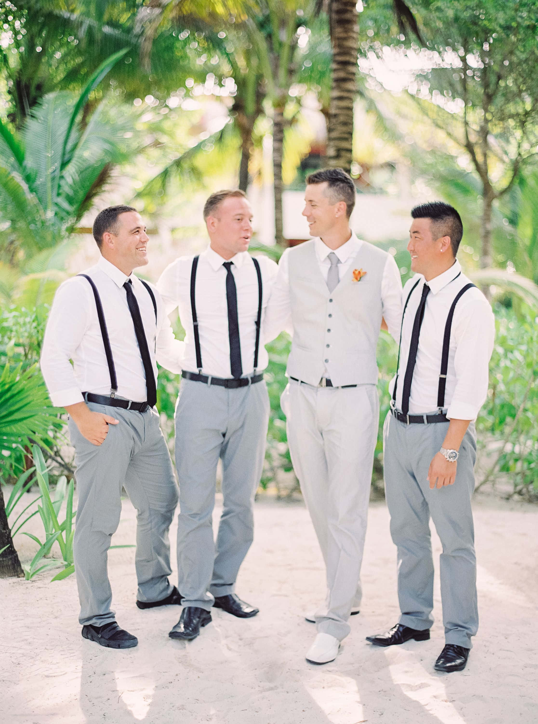 Groomsman 桌布 壁紙 — 四位伴郎穿著白襯衫、黑色吊帶和灰色褲子，在陽光明媚的海灘棕櫚樹下一起大笑。