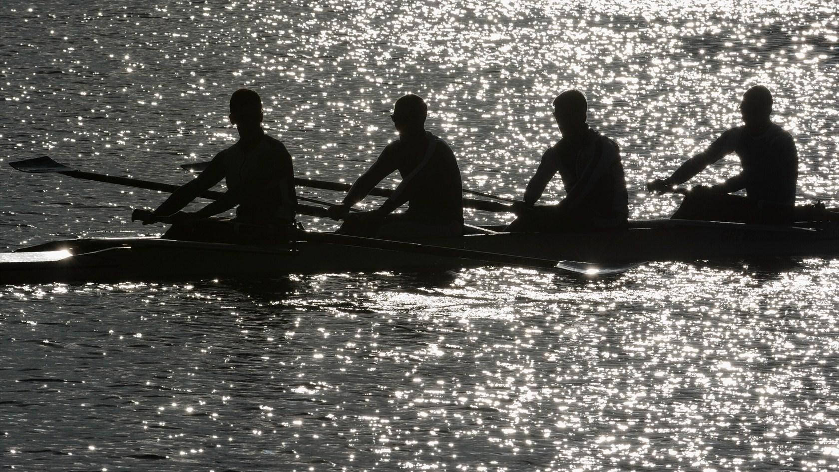 Rowing 桌布 壁紙 — 四位划艇選手以剪影形式滑過水面，水面閃爍著金色的陽光倒影。