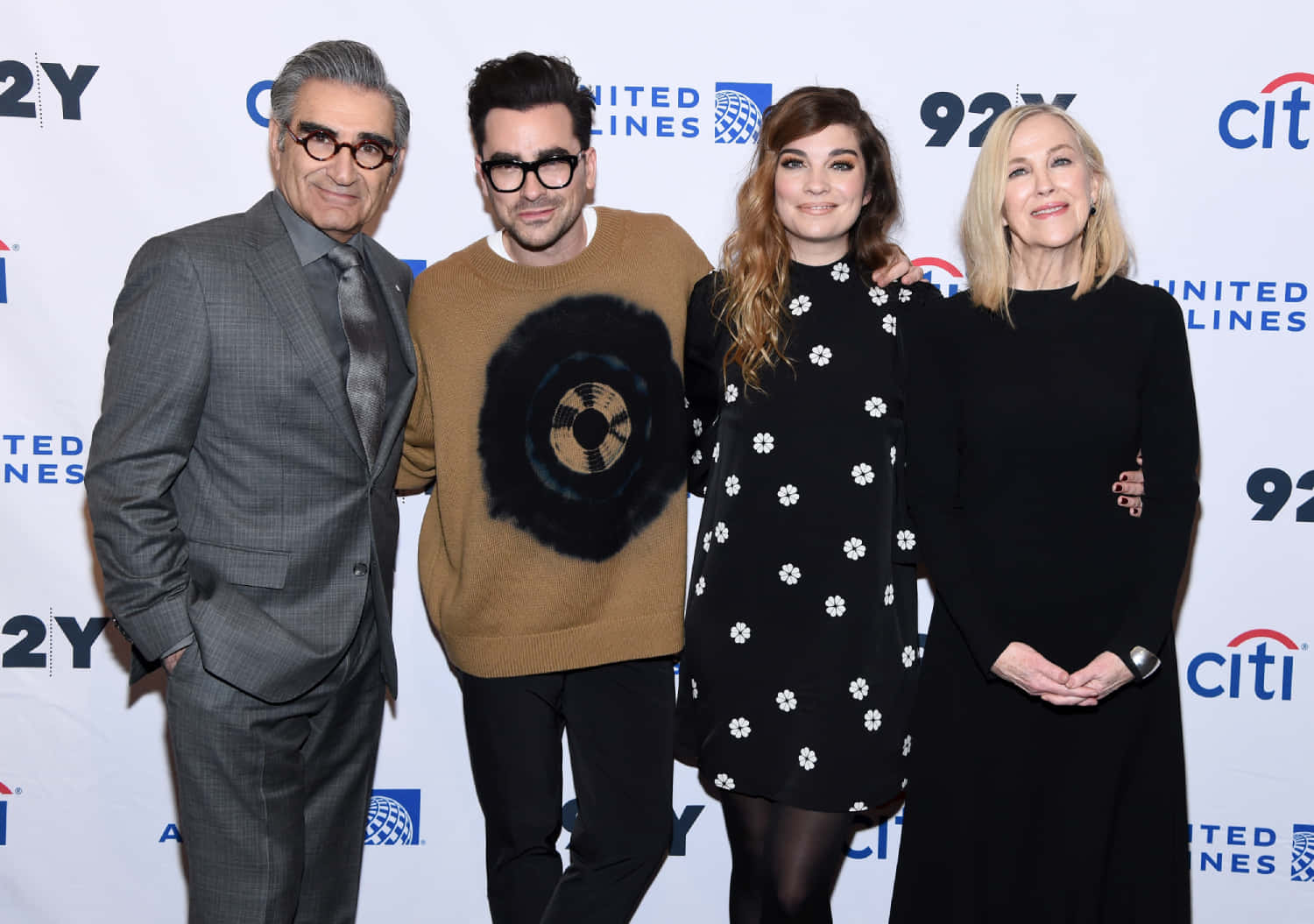 Eugene Levy 桌布 壁紙 — 四位名人一起在品牌活動背景前擺姿勢，背景有標誌和微笑表情。