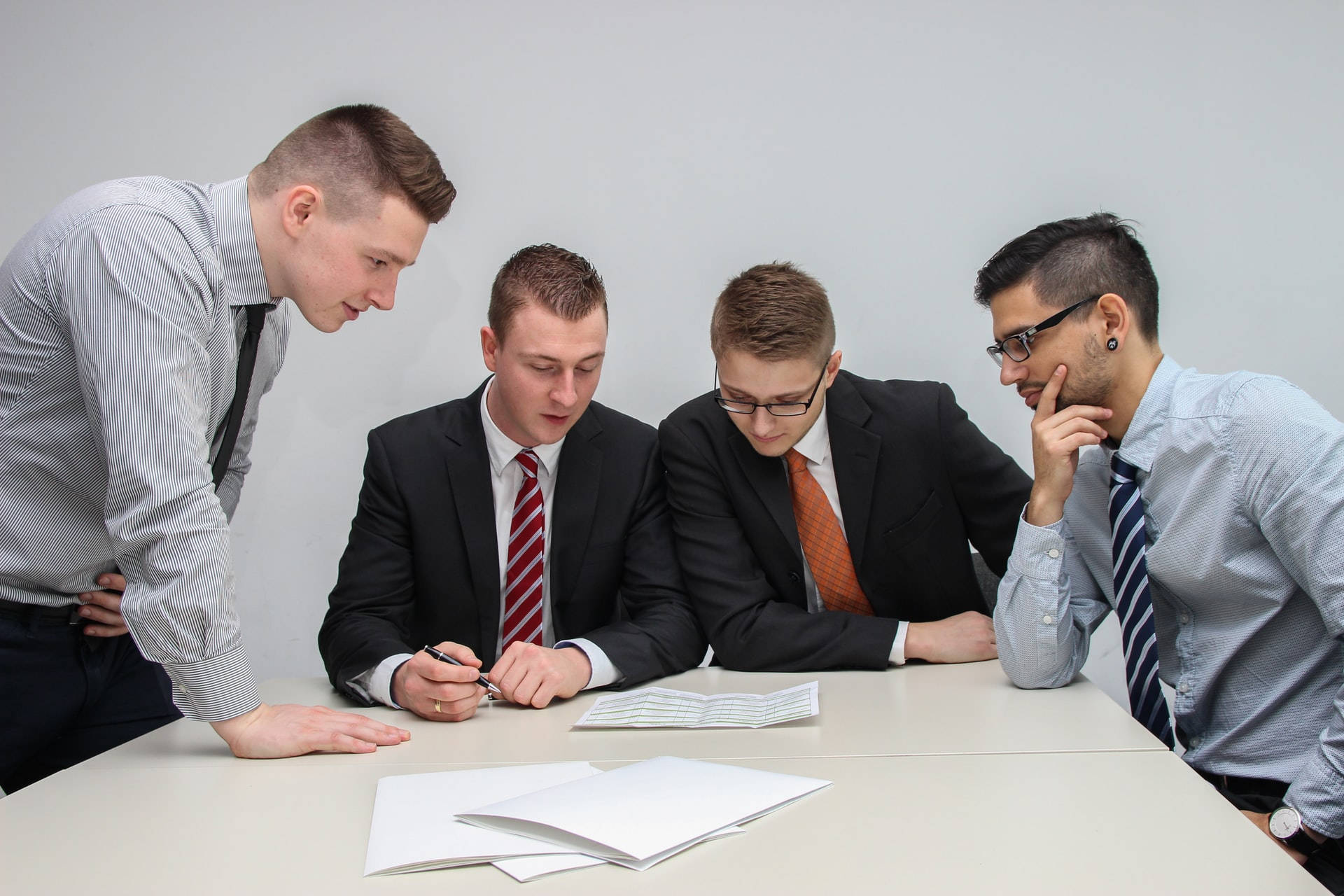job 桌布 壁紙 — 四位商業專業人士在簡約風格的辦公室環境中俯身查看文件。