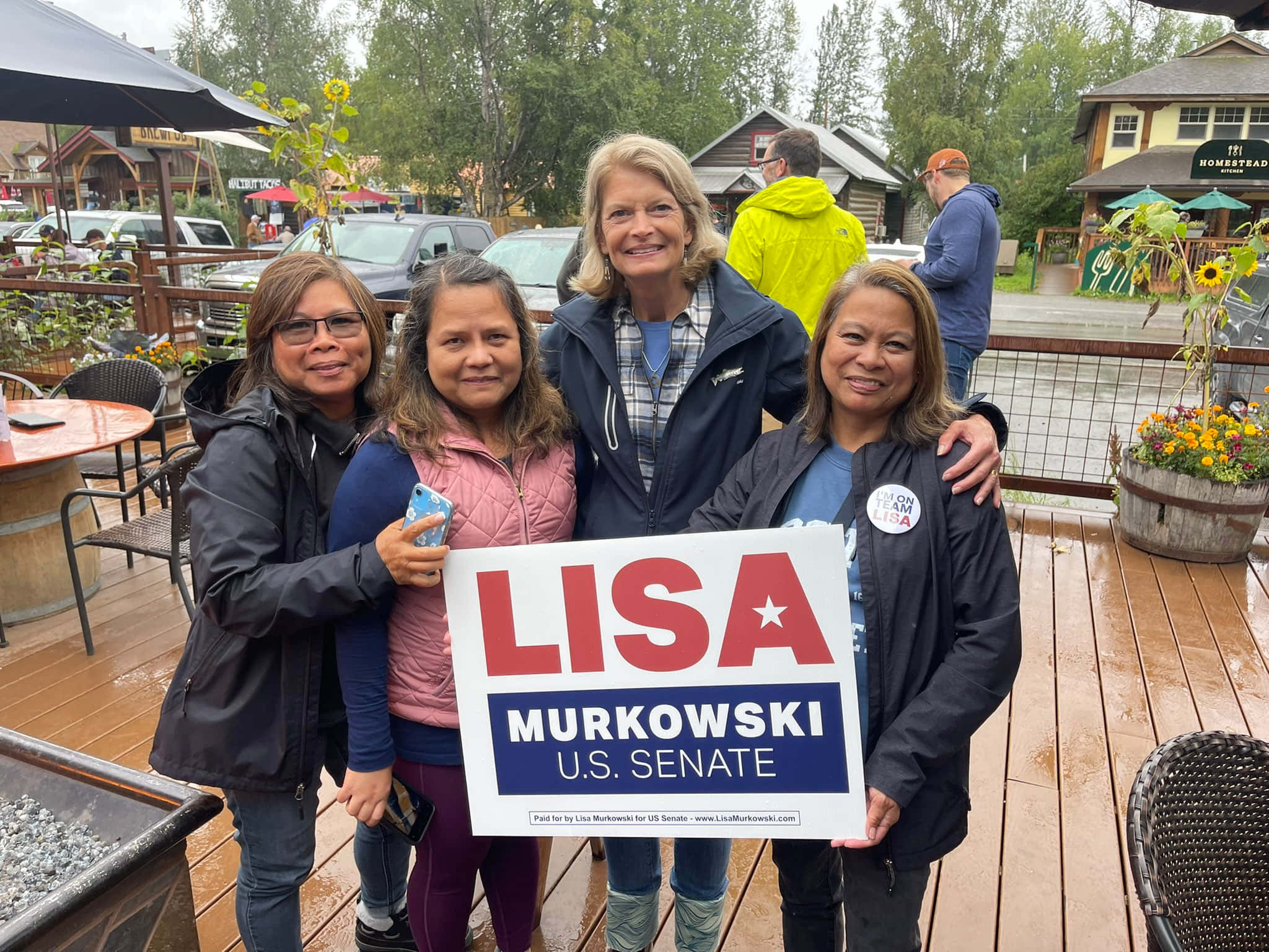 人物 桌布 壁紙 — 四位女士在潮濕的木甲板上一起微笑，手持「Lisa Murkowski U.S. Senate」競選標語牌。