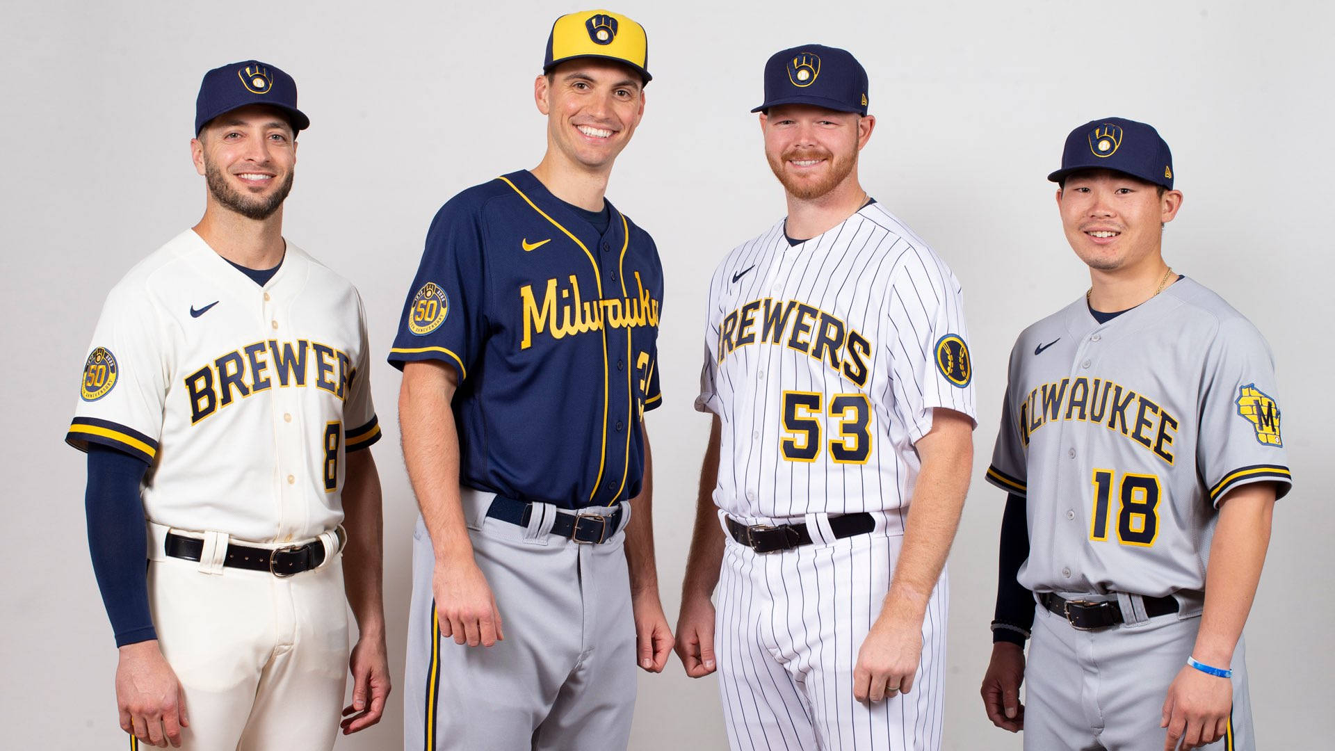 Brewers 桌布 壁紙 — 四位密爾瓦基釀酒人棒球球員在攝影棚內穿著不同顏色配搭的球隊球衣，在純白色背景前擺姿勢。