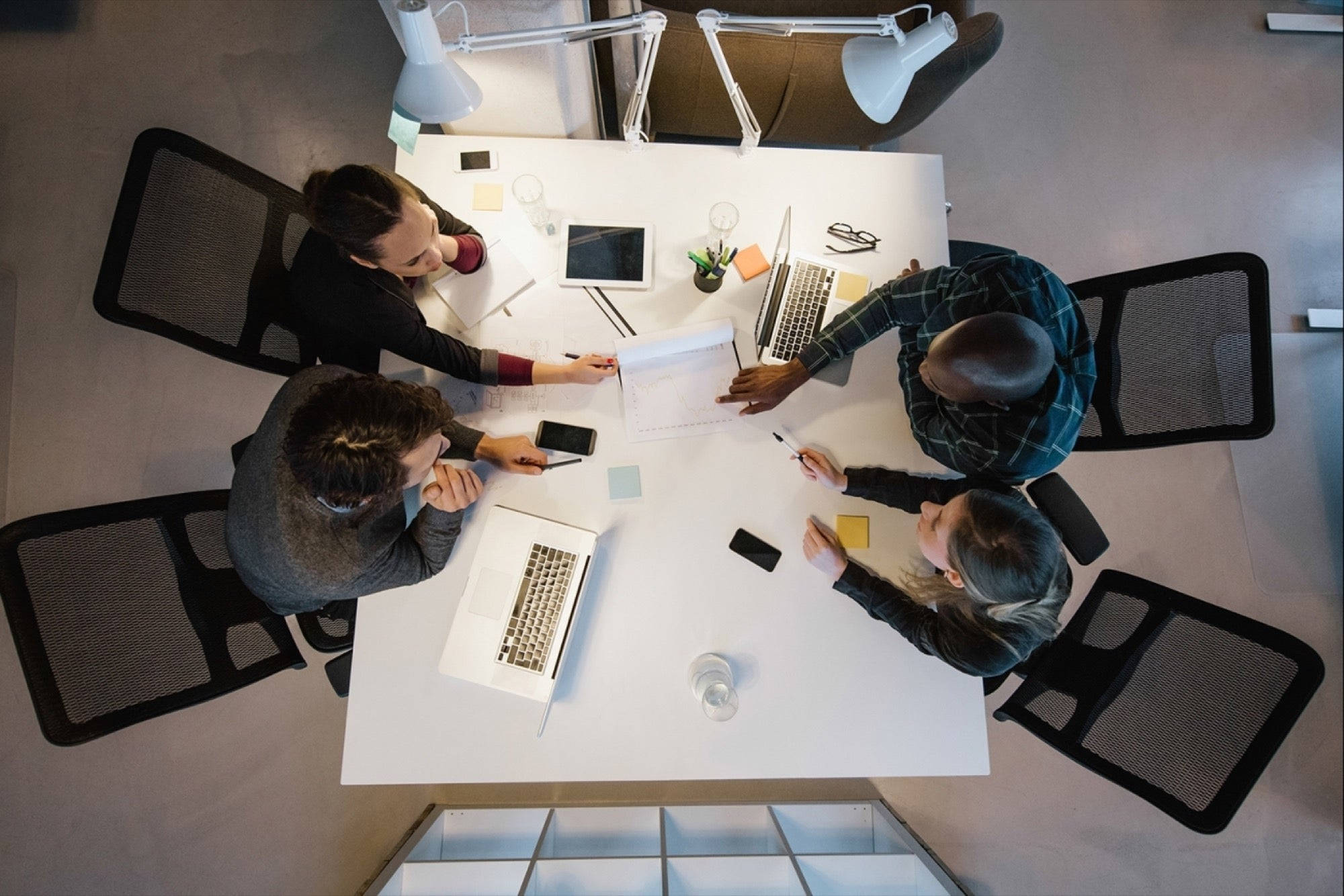 Teamwork 桌布 壁紙 — 四位專業人士在現代辦公室中從俯視角度圍繞白色會議桌協作。